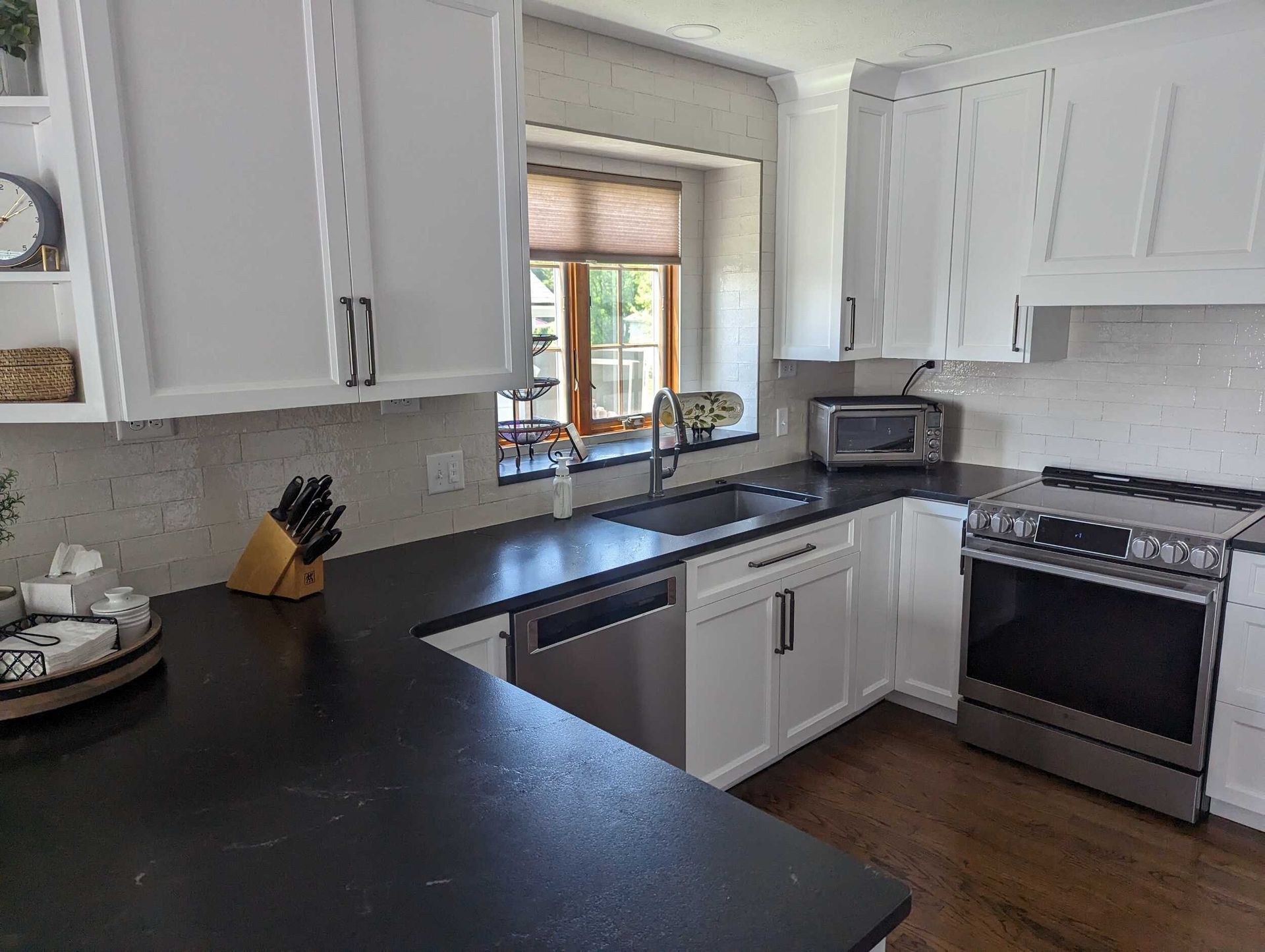 White kitchen with dark countertops, stainless steel appliances, and a window with blinds.