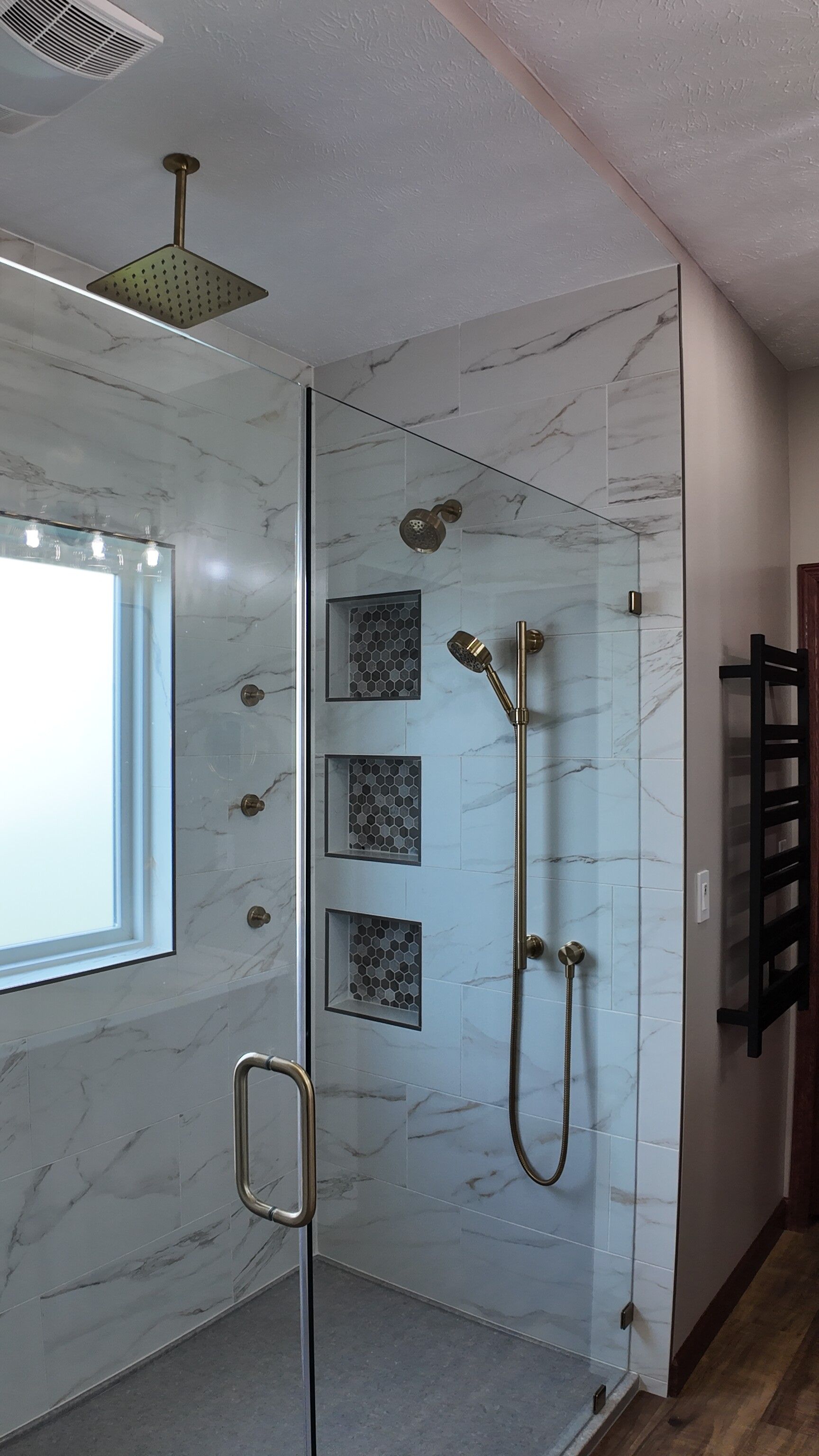 Modern shower with marble-look tile, glass door, and gold fixtures. Three recessed shelves with stone accents.