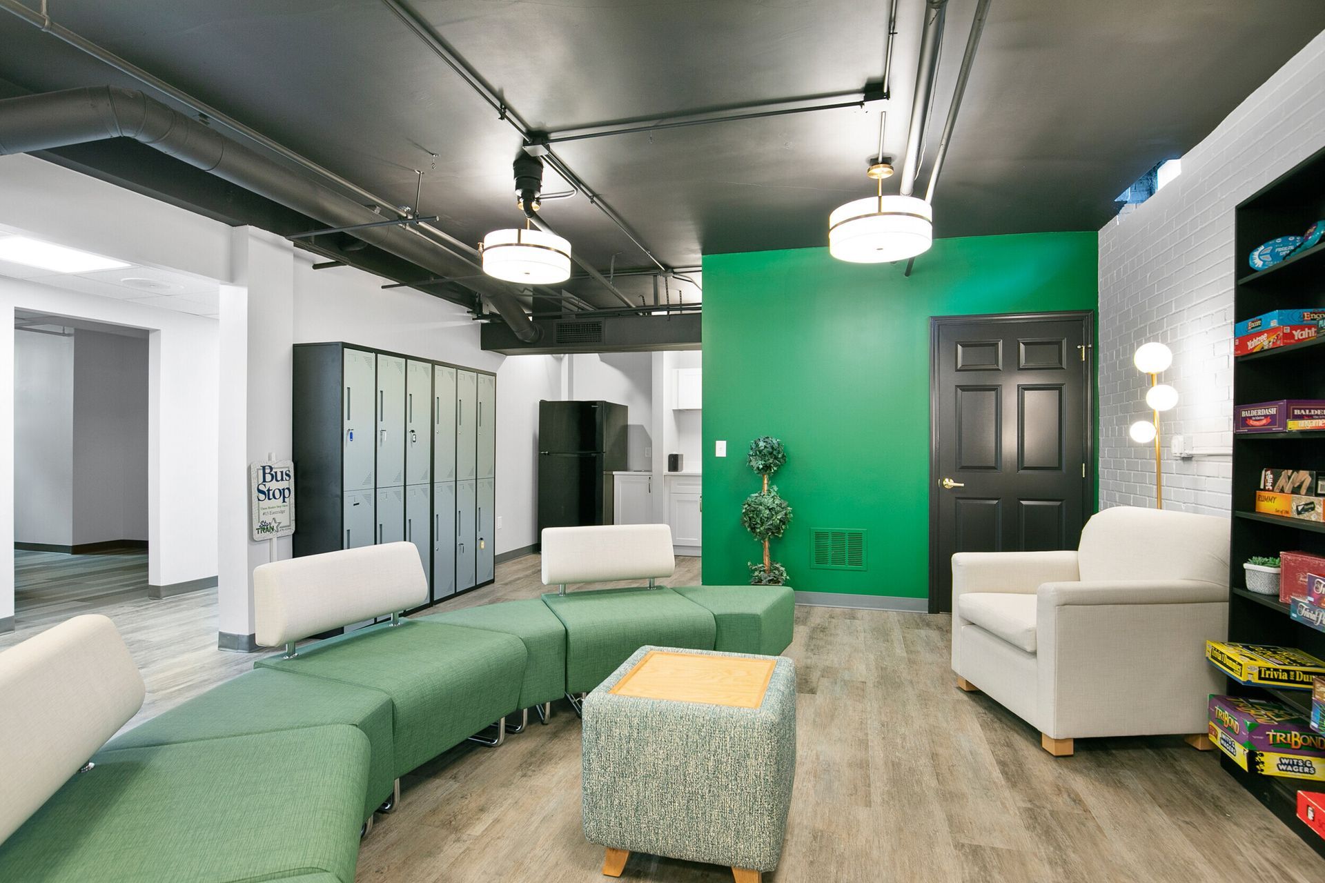 Lounge area with green seating, lockers, a green accent wall, and a bookshelf with toys.