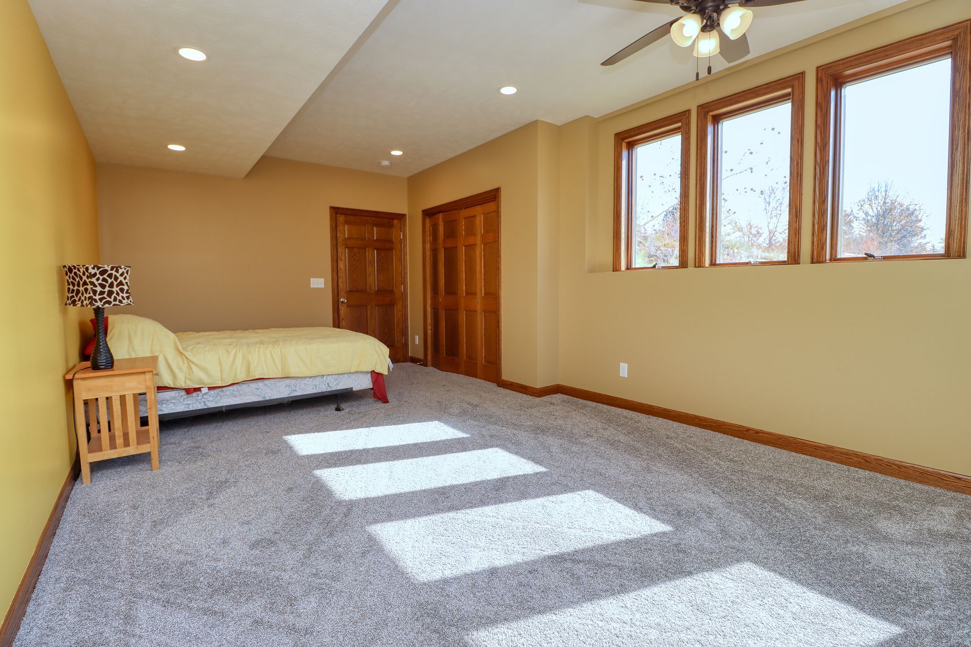 Bedroom with a bed, nightstand, wood doors, windows, light gray carpet, and yellow walls.