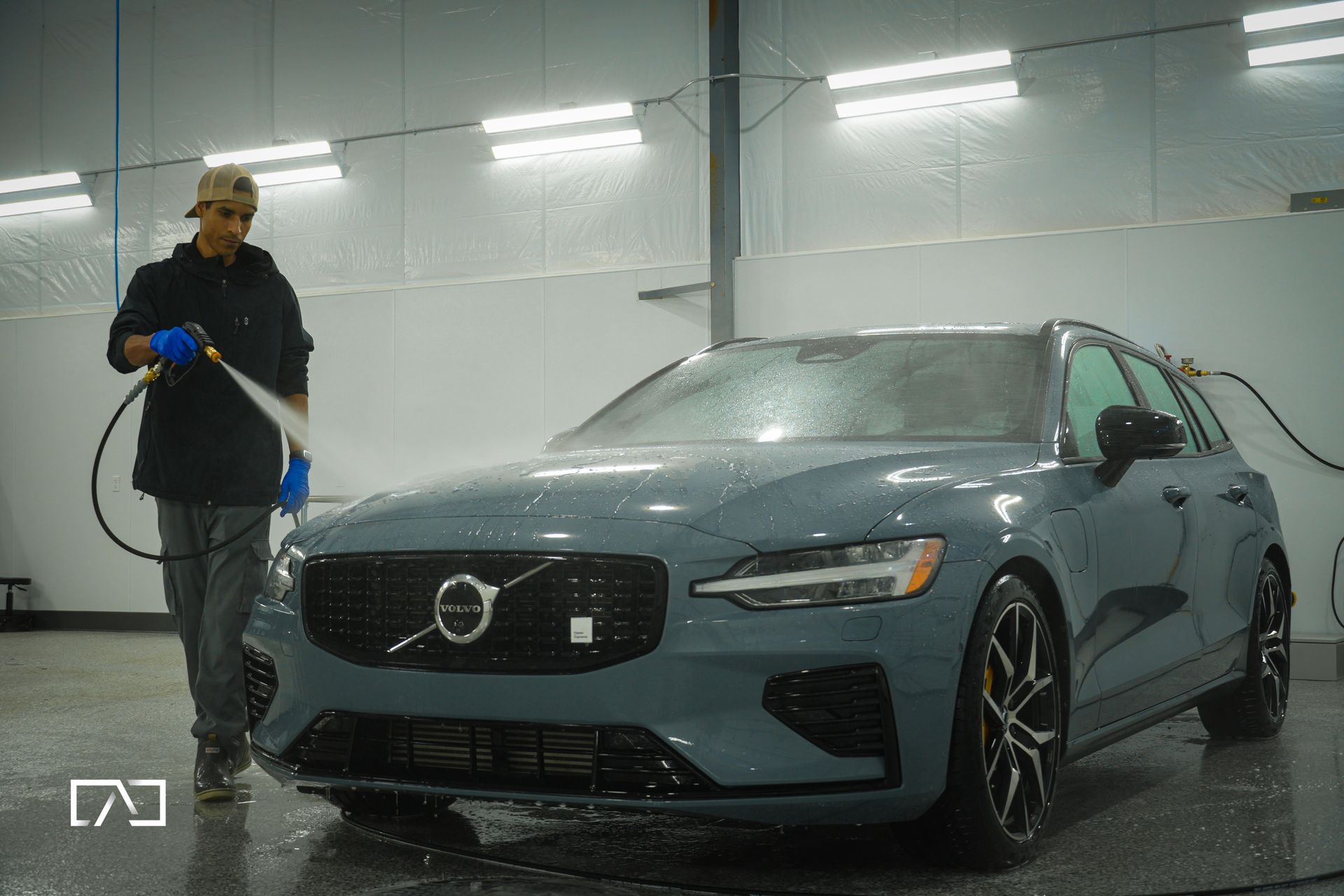 Man washes a black Toyota truck with water. Outdoors, sunlight.