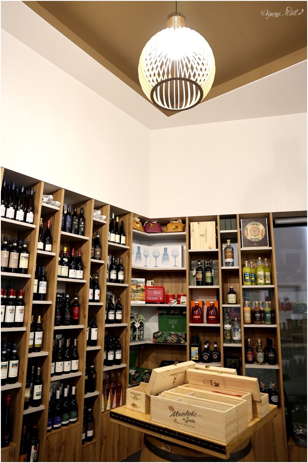 Una stanza con scaffali in legno pieni di bottiglie di vino, un'esposizione di casse di legno e un lampadario sferico moderno.