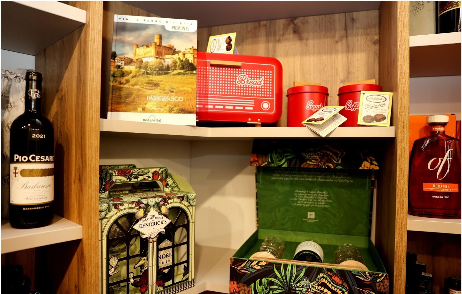 Uno scaffale con vino Pio Cesare, un libro, una radio rossa in stile vintage, due barattoli rossi e scatole regalo.