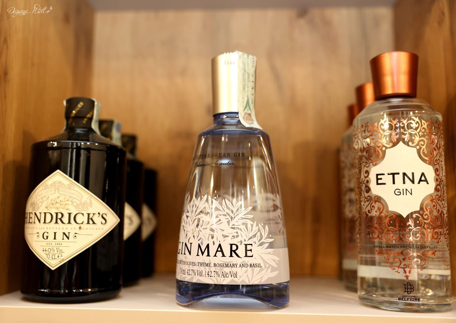 Tre bottiglie di gin su uno scaffale di legno: Hendrick's Gin, Gin Mare ed Etna Gin.