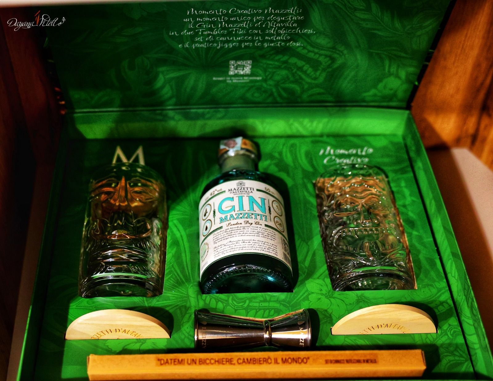 Una confezione regalo verde contenente una bottiglia di Gin Mare, due bicchieri decorati, un misurino e una bacchetta di legno per mescolare.