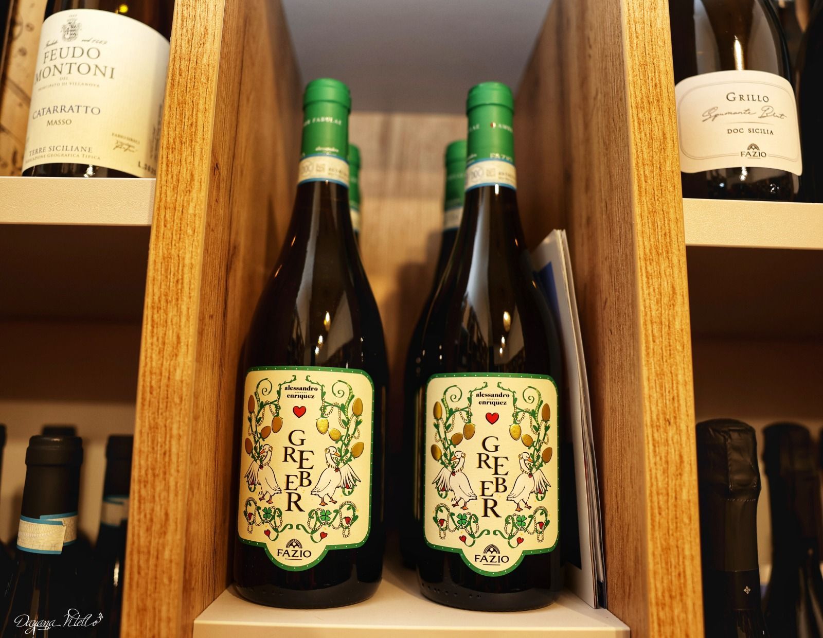 Due bottiglie di vino Gregoletto con etichette botaniche decorative esposte su uno scaffale di legno.