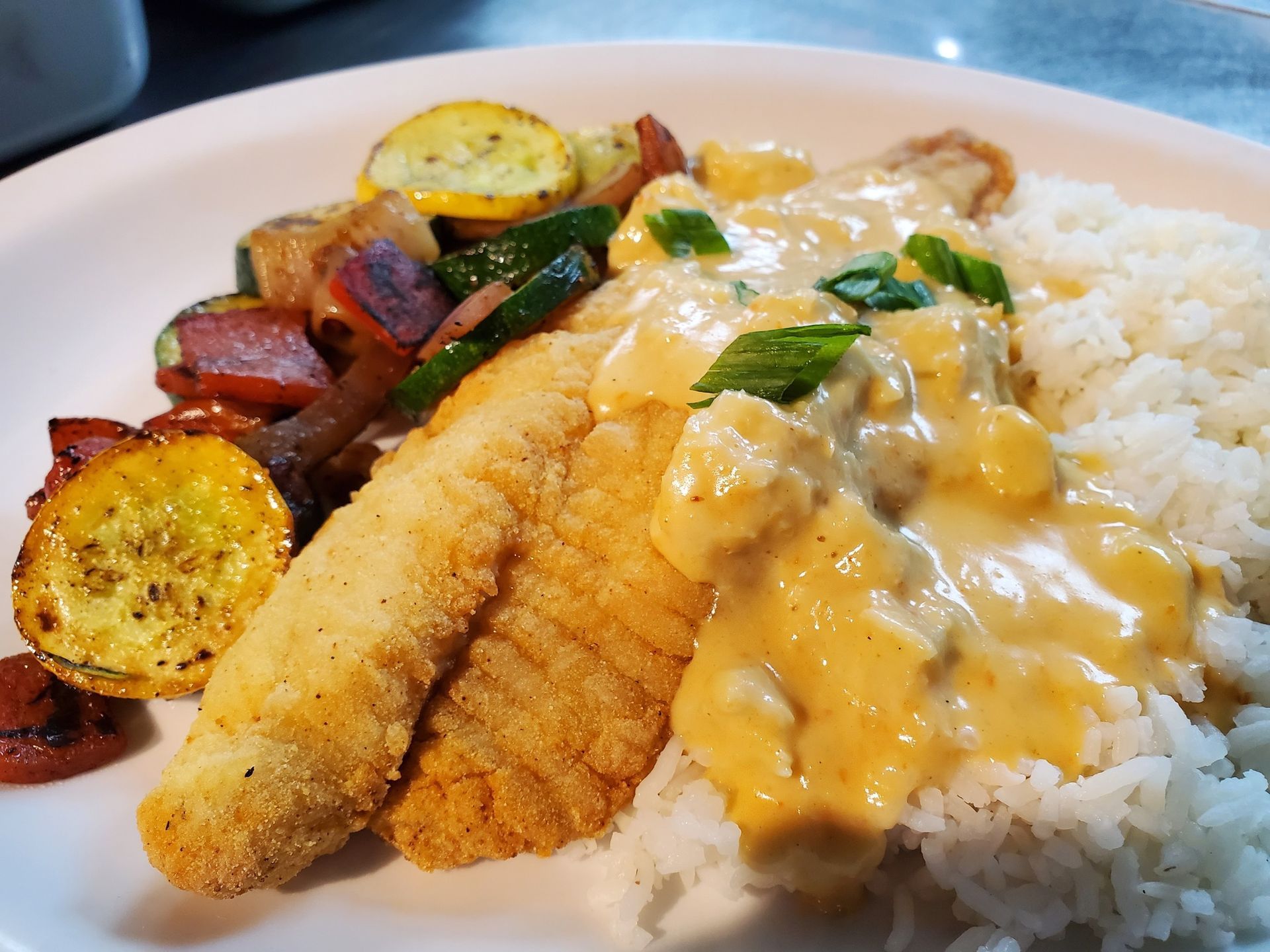 Plate of fried fish with creamy sauce, rice, and roasted vegetables.
