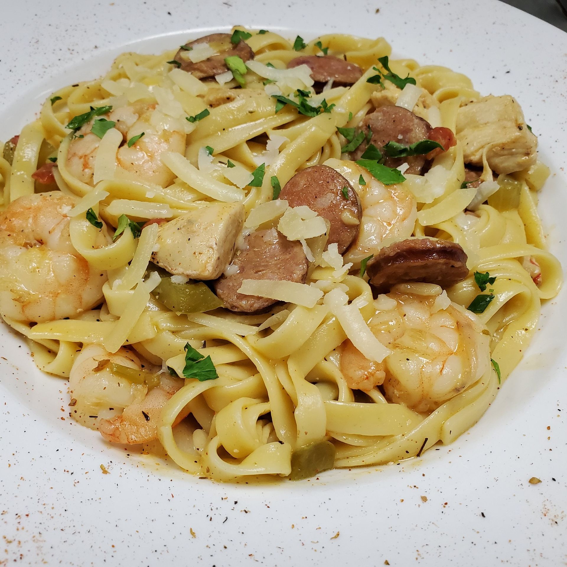Fettuccine pasta with shrimp, chicken, sausage, and cheese in a white bowl.