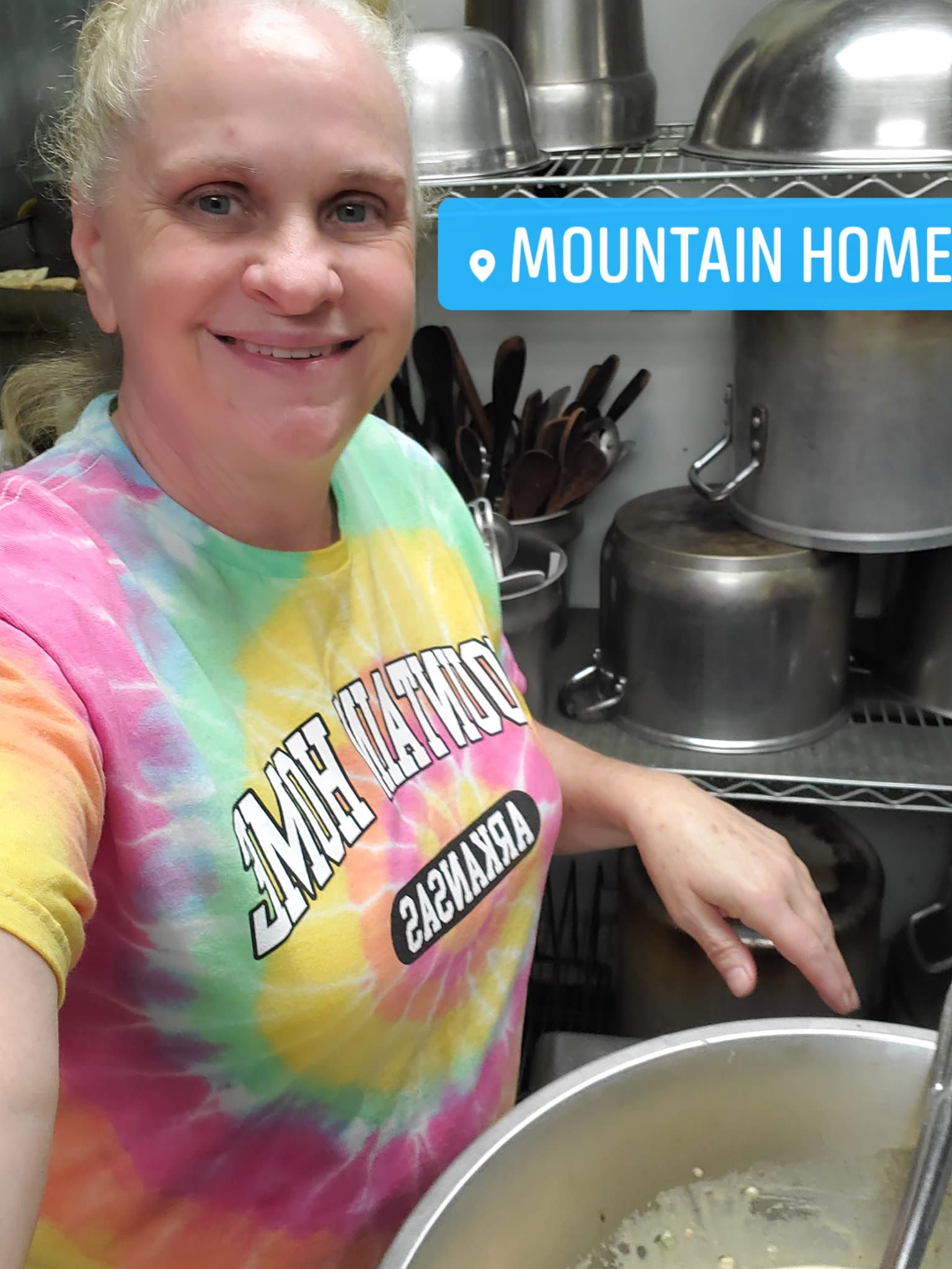 Woman in tie-dye shirt smiles near a pot, 