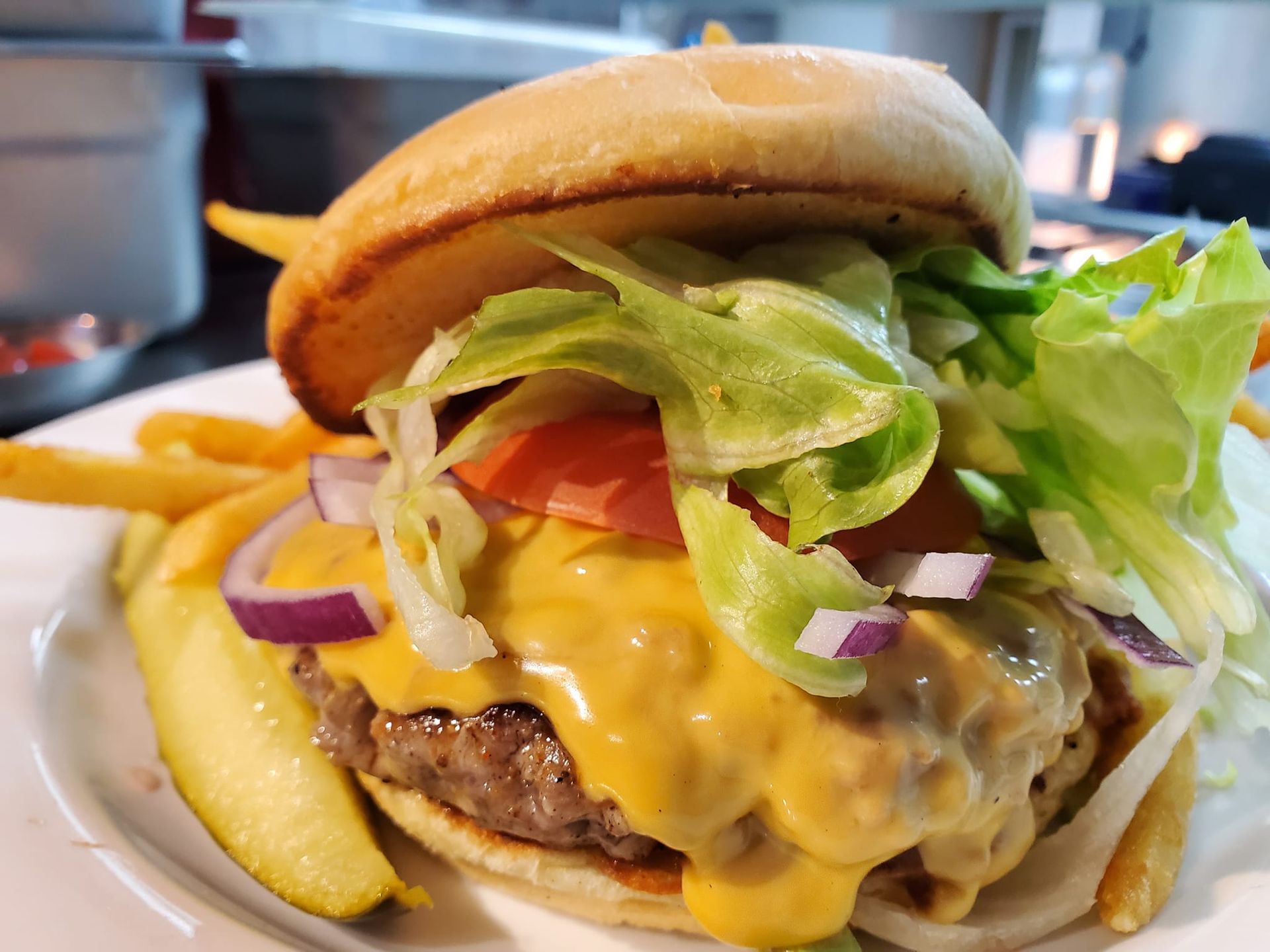 Cheeseburger with melted cheese, lettuce, tomato, onion, and a pickle, served with fries.