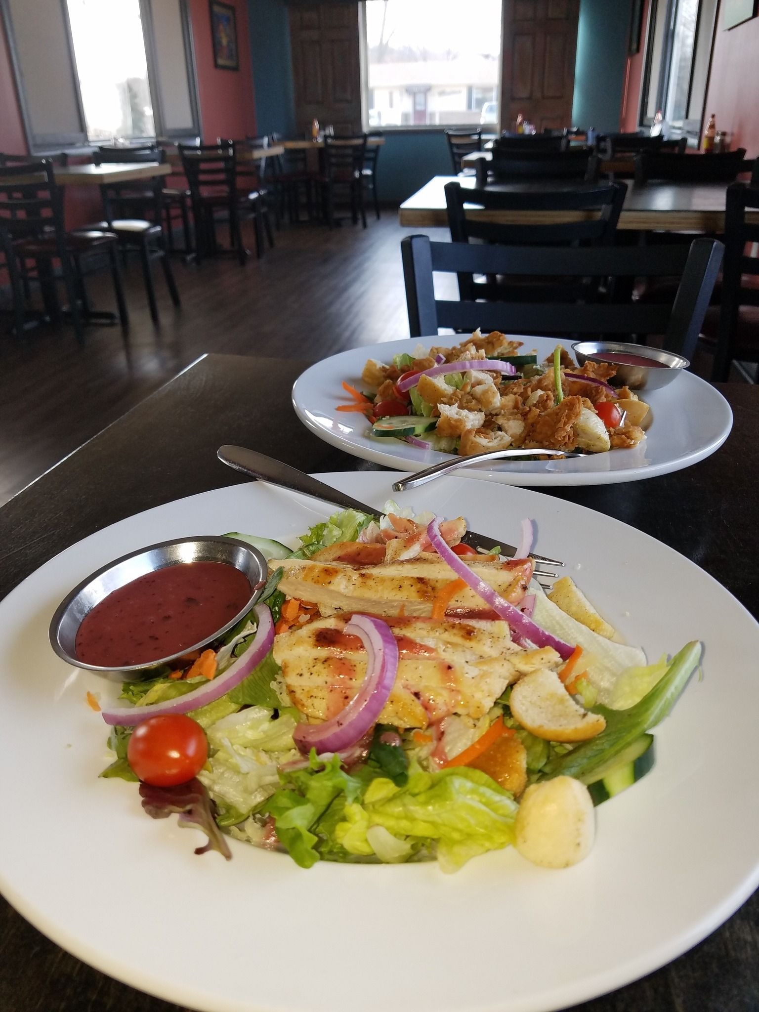 Two plated salads with chicken in a restaurant. One with a red dressing and another with a sweet glaze.