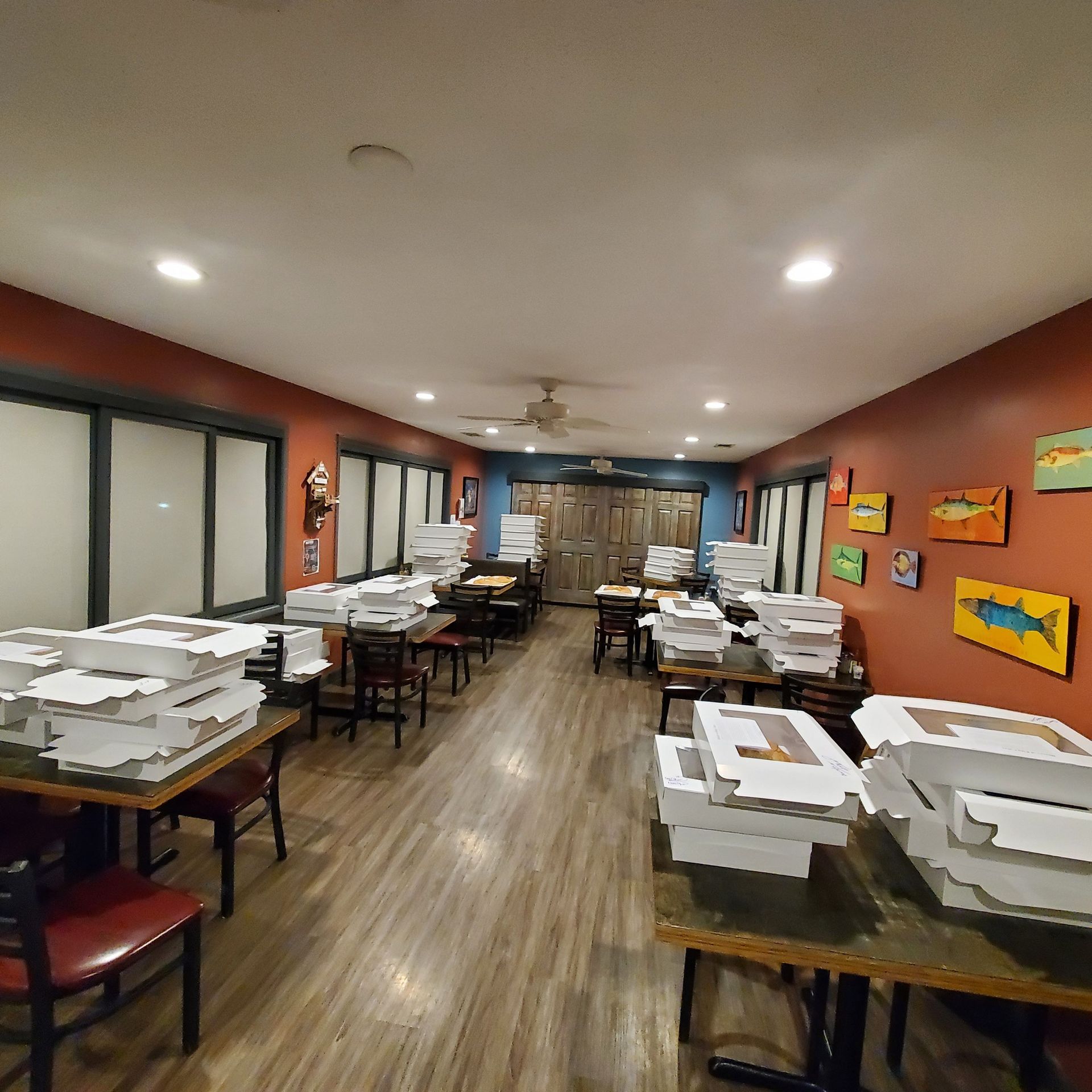 Restaurant interior with pizza boxes on tables, red walls, wooden floor, and a few patrons.