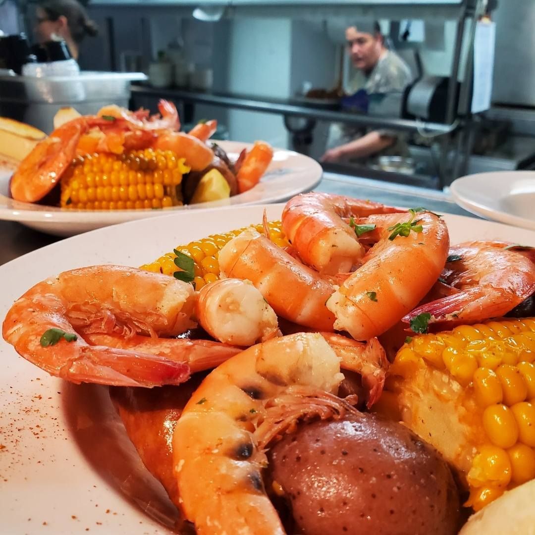 Shrimp boil on plates with corn and potatoes; chef in background of the kitchen.