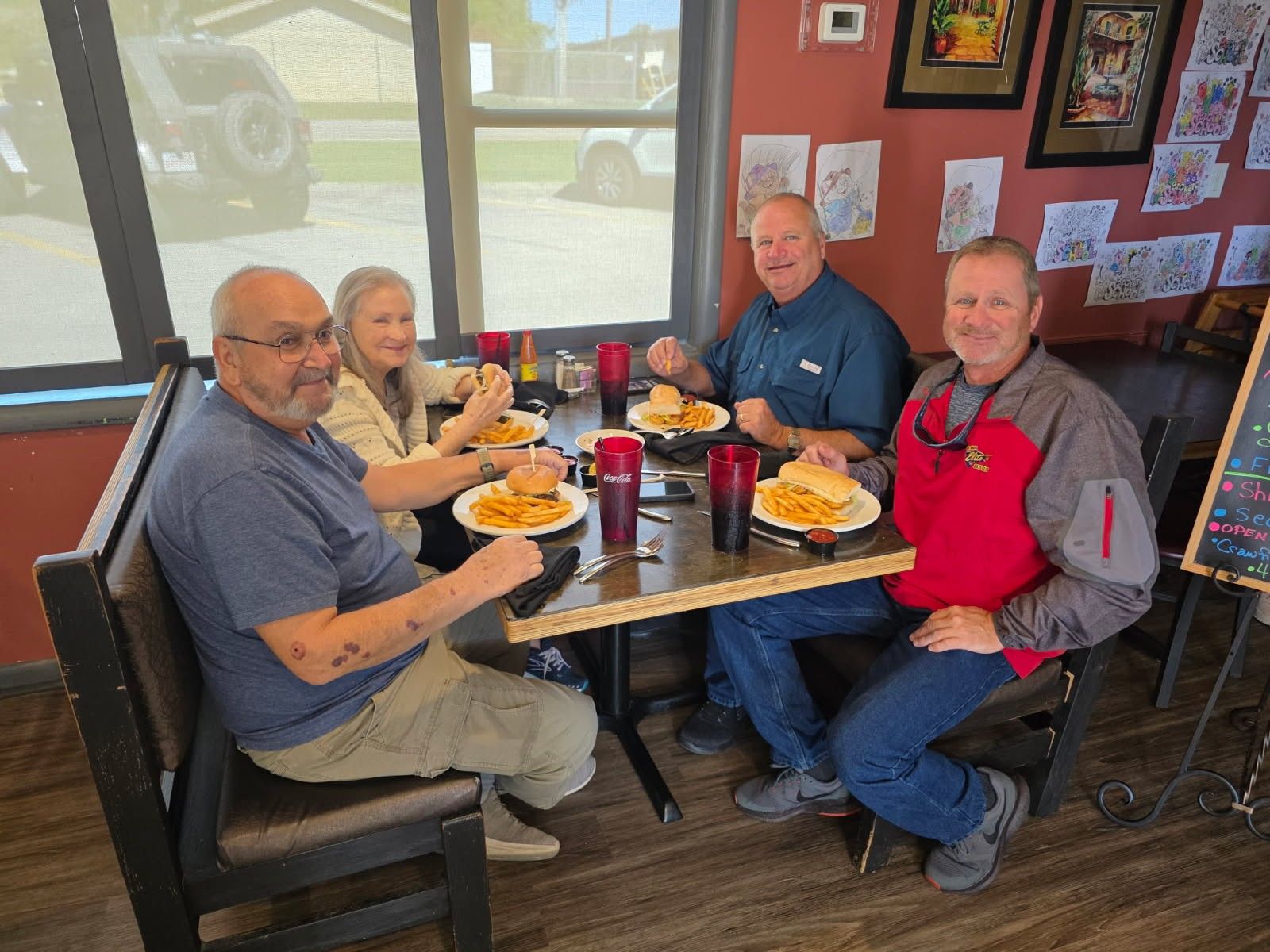 Four people eating at a table in a restaurant. They're eating burgers and fries.