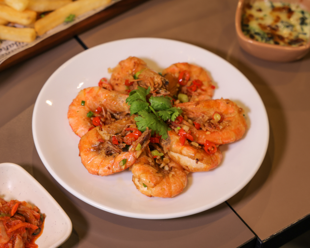 Plate of cooked shrimp garnished with cilantro. Other dishes are in the background.