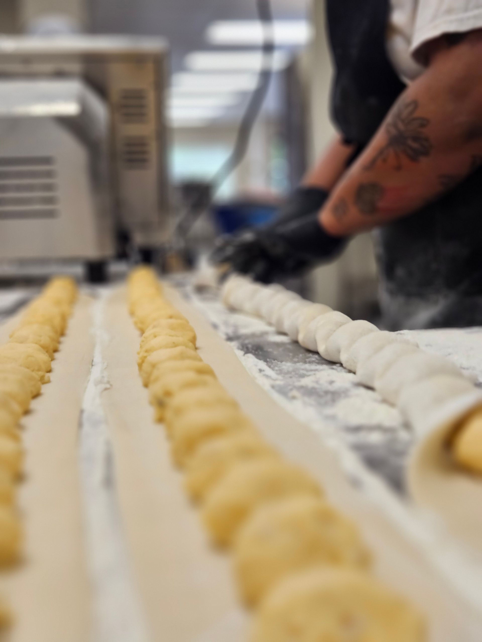 Two people are working in a kitchen with trays of pierogi