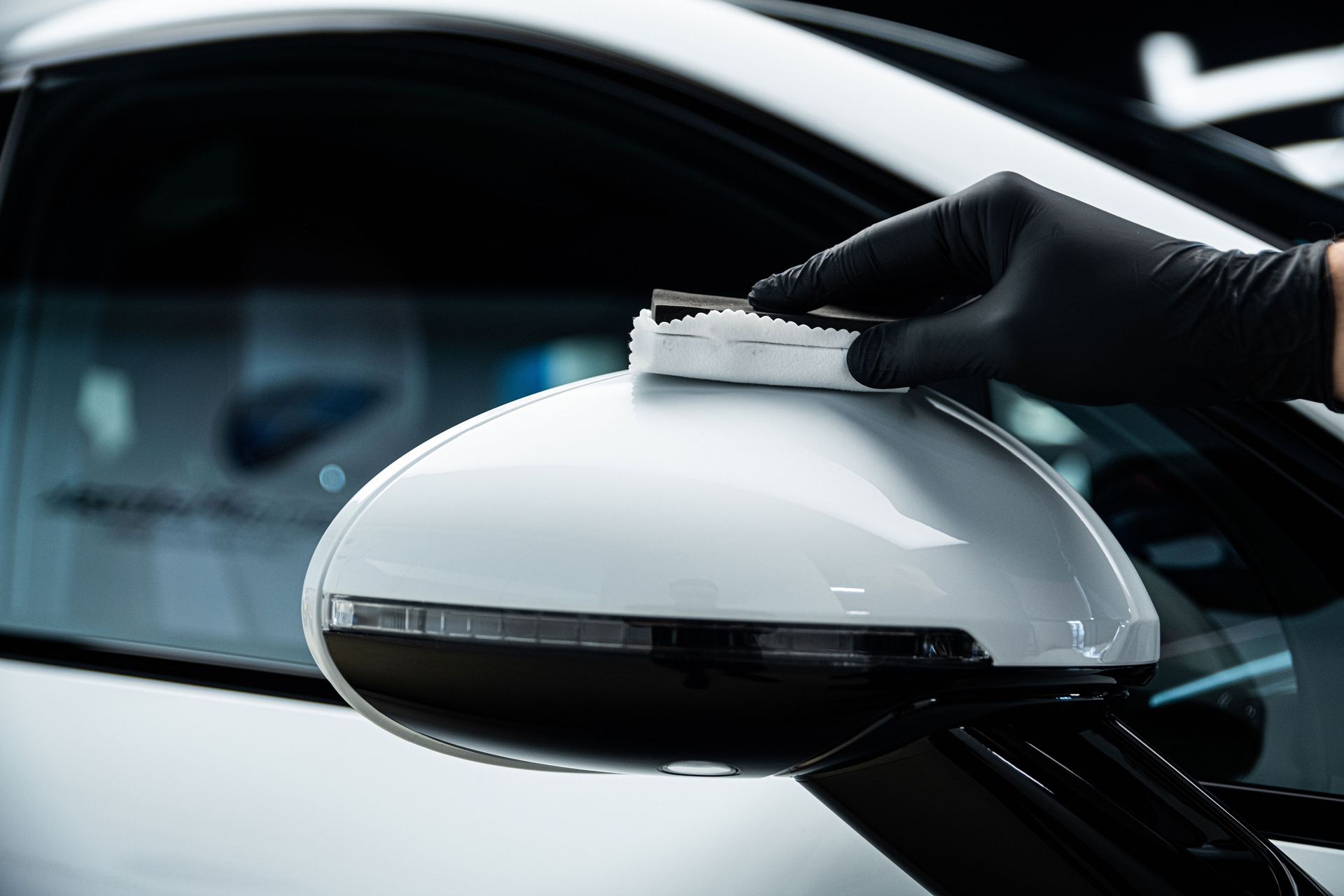 Gloved hand applying ceramic coating to a white car's side mirror.