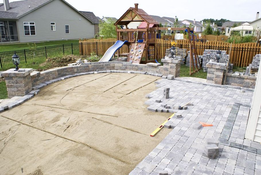 Backyard with a large concrete patio, stone retaining walls, and a wooden playset with slide
