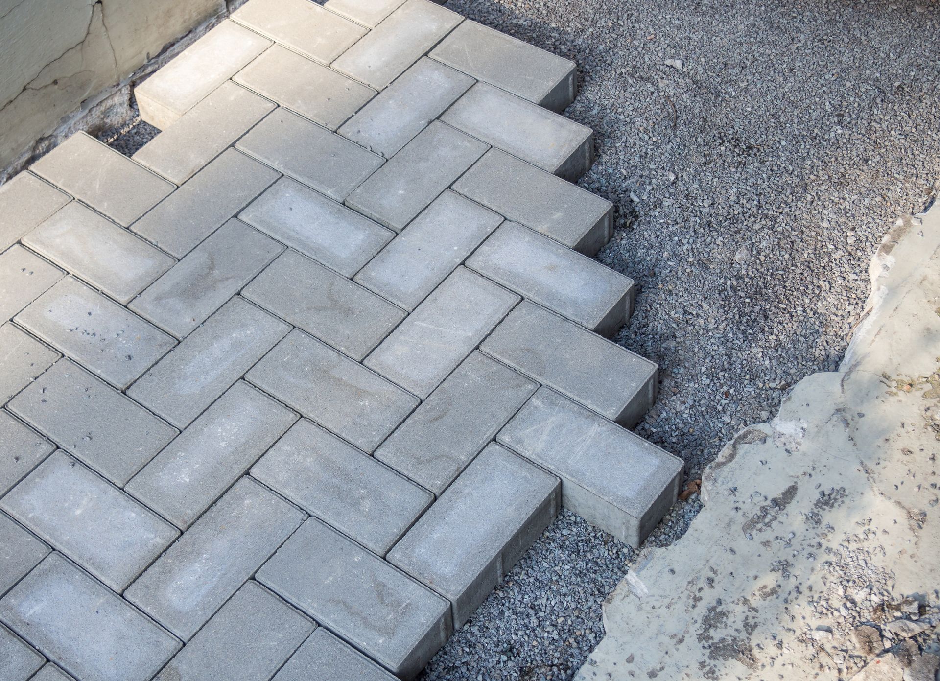 Herringbone pattern of gray paving stones next to gravel and concrete.
