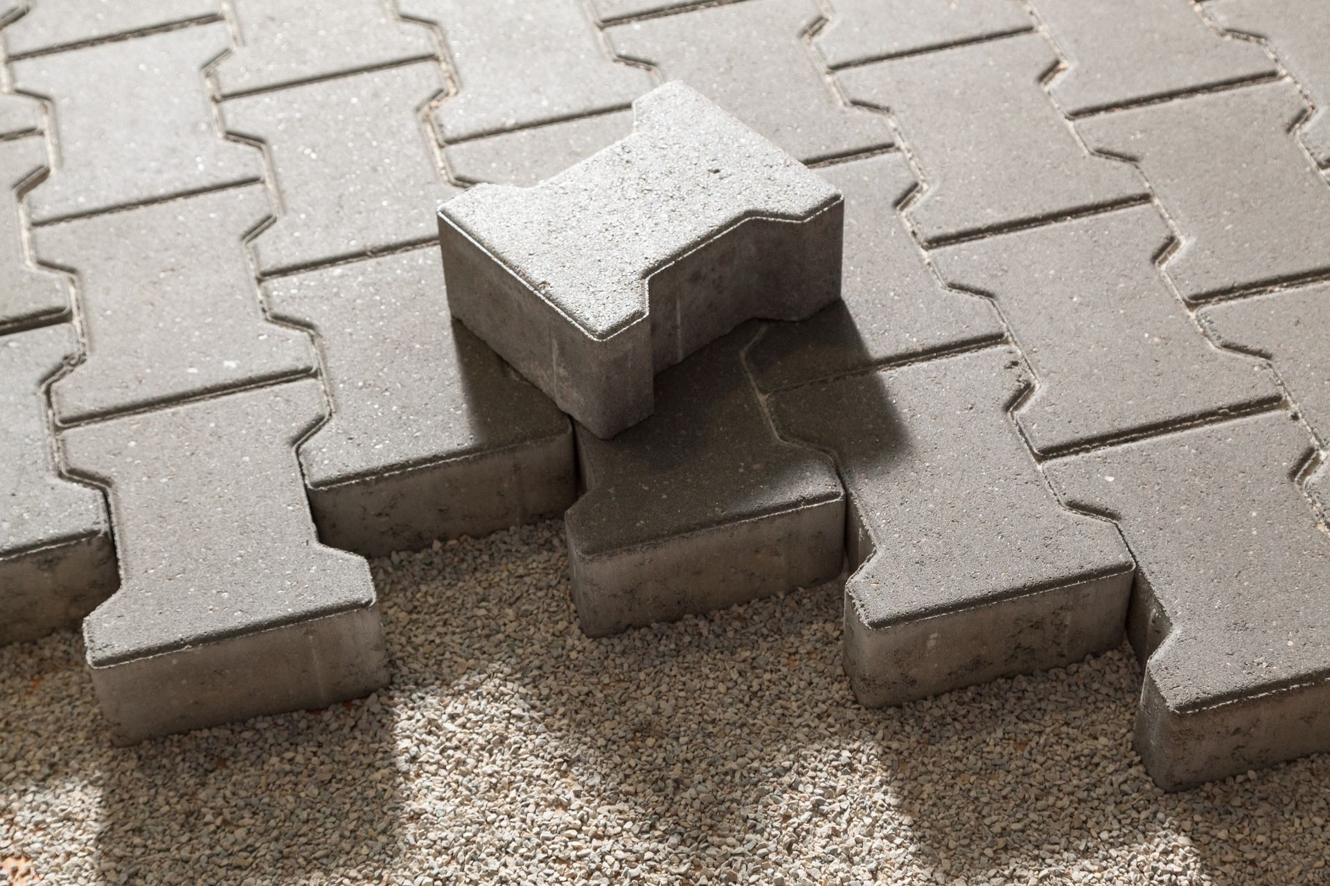 Gray interlocking pavers on gravel, one paver slightly raised.