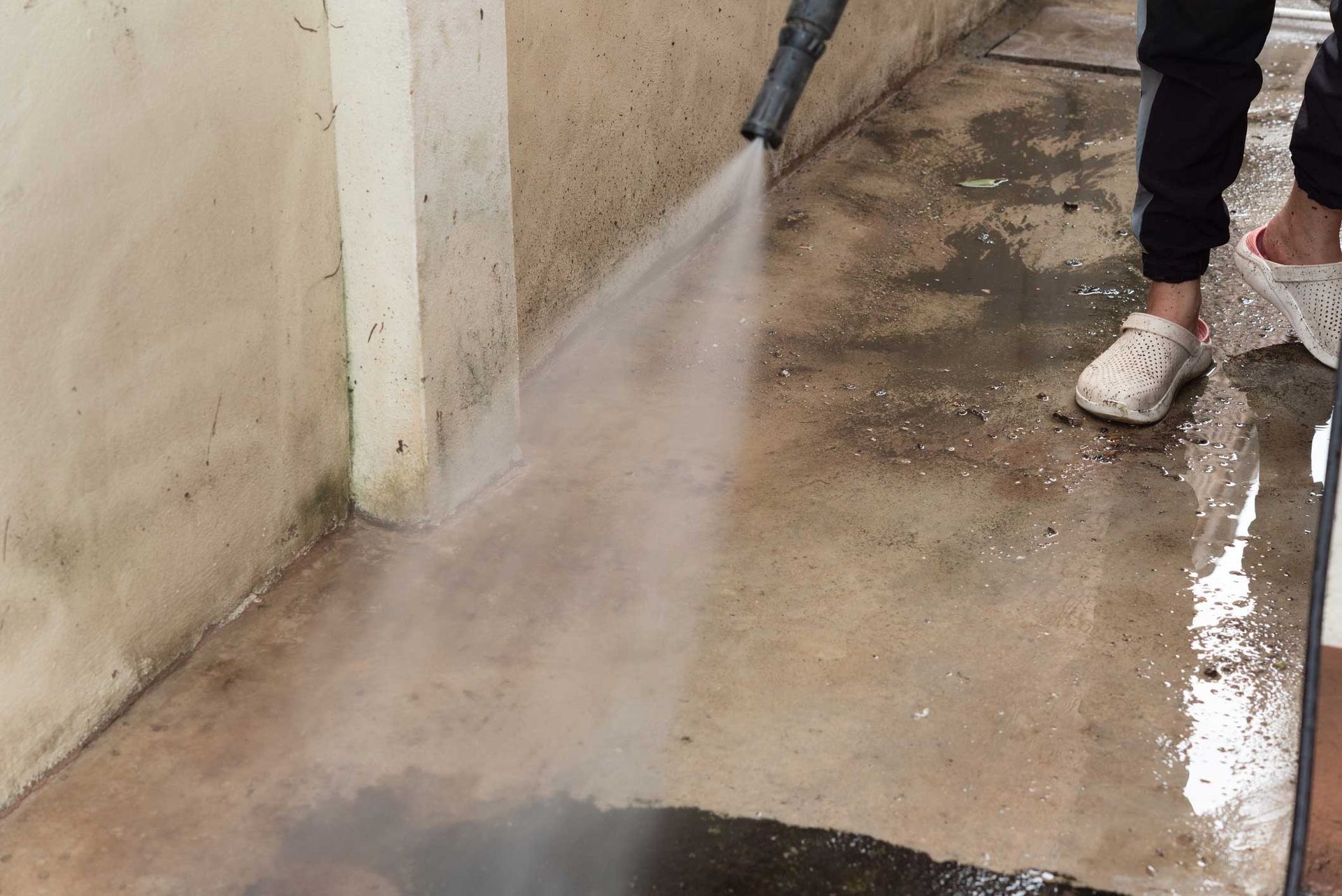 Person power washing a concrete surface near a wall, creating a mist of water.