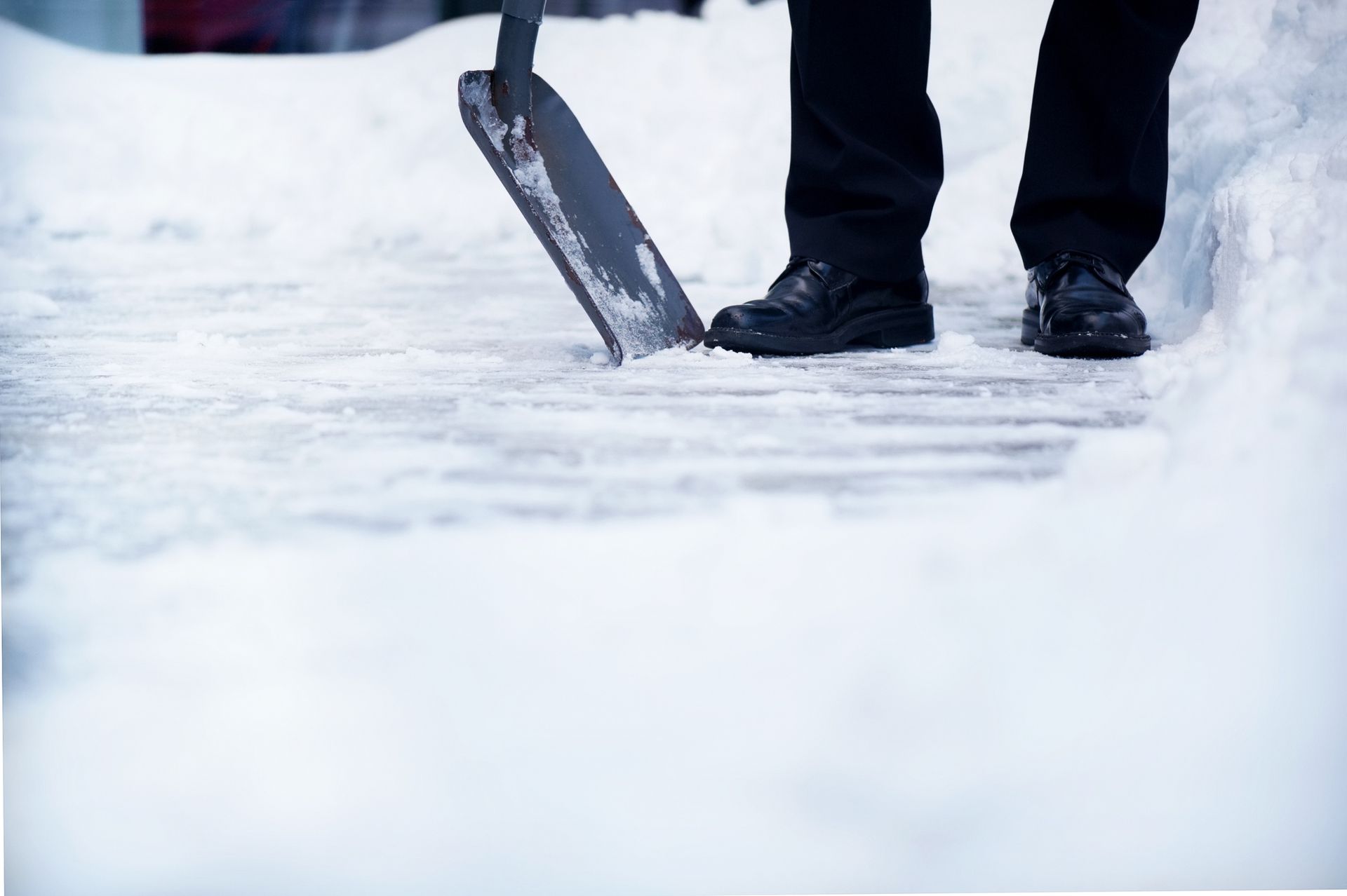 Person shoveling snow on a walkway. Black shoes and a shovel in a snowy setting.