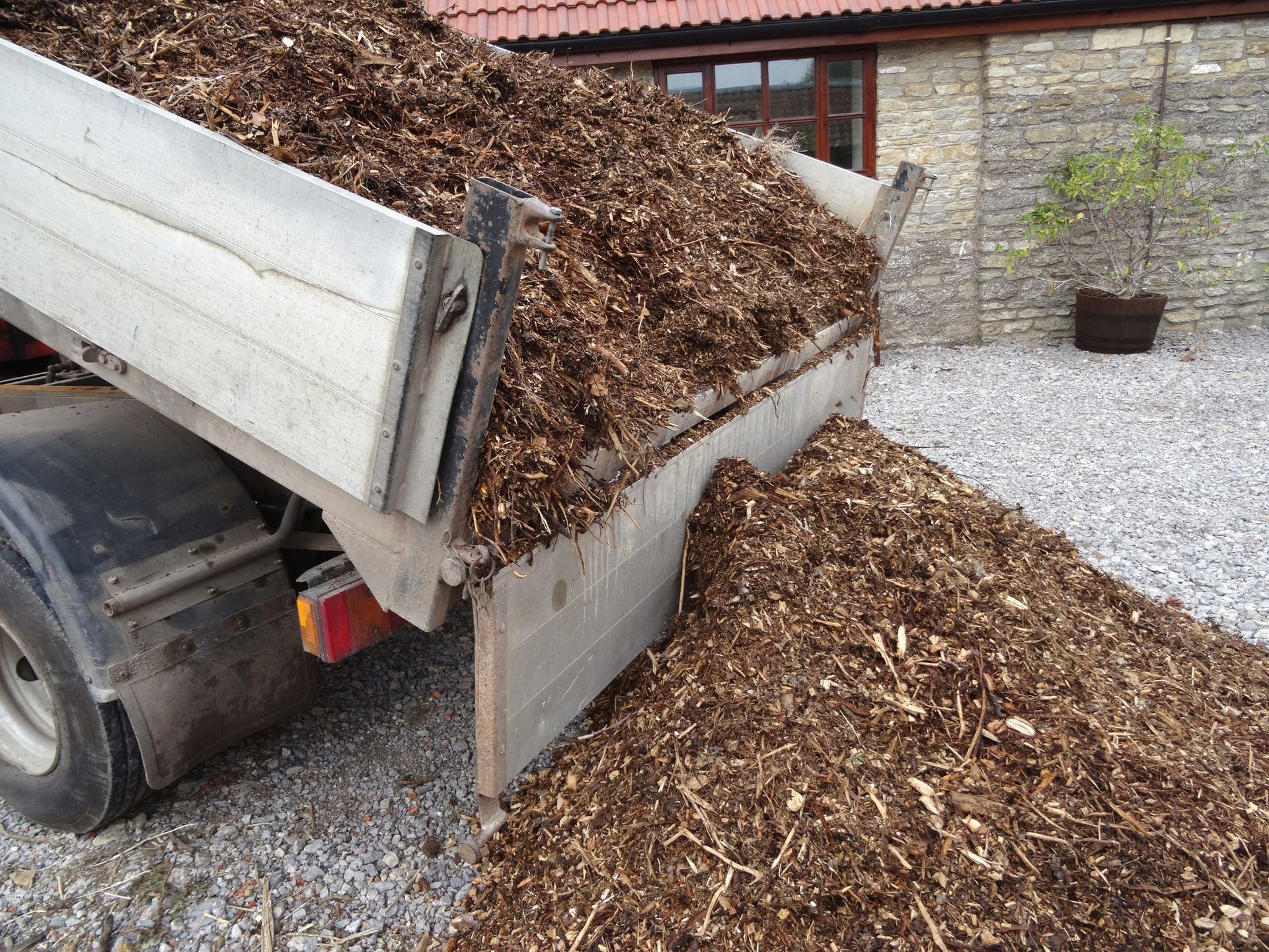 Wood chips being unloaded from a truck onto a gravel driveway.