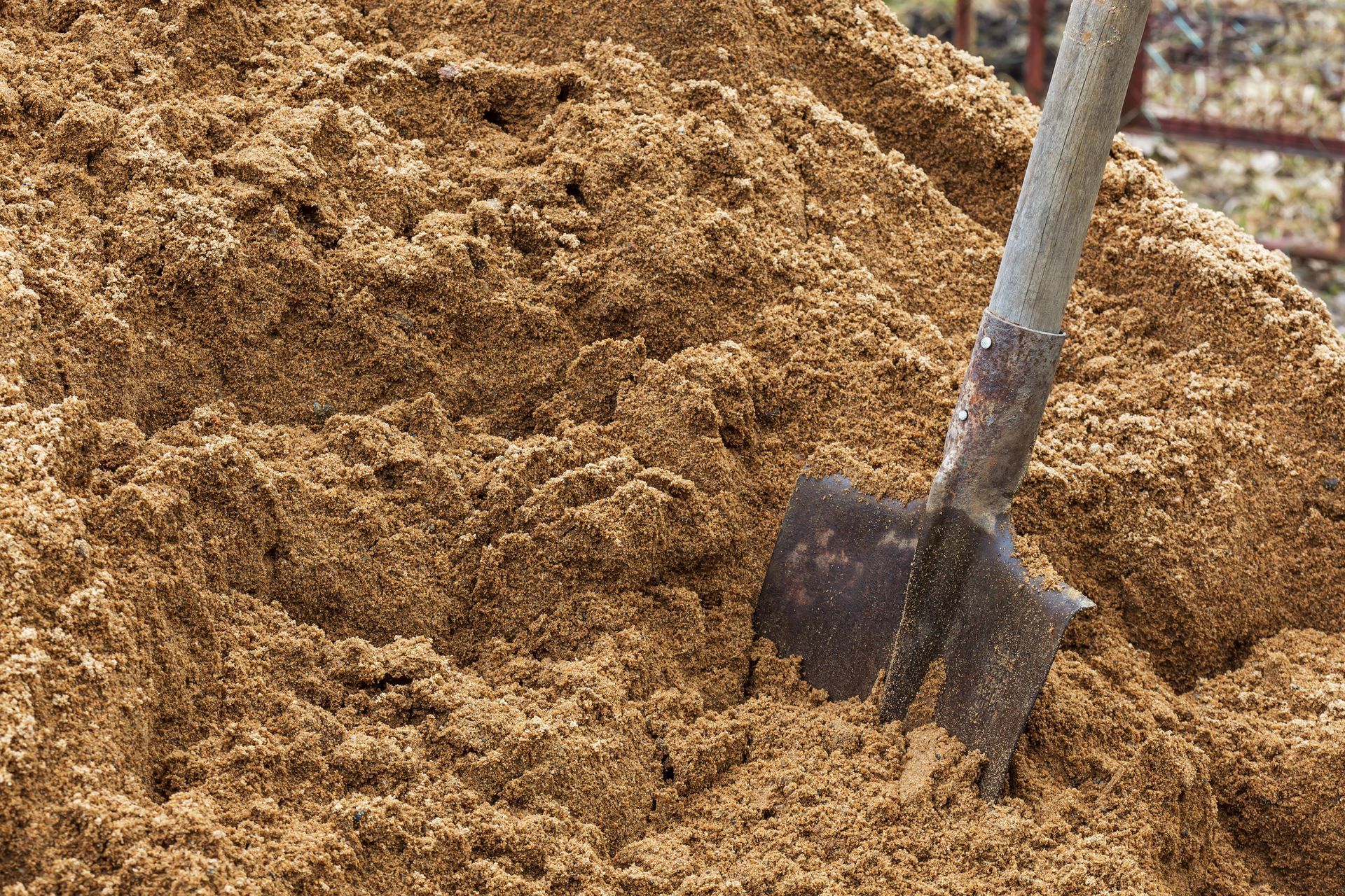 A pile of brown sawdust with a shovel stuck in it.