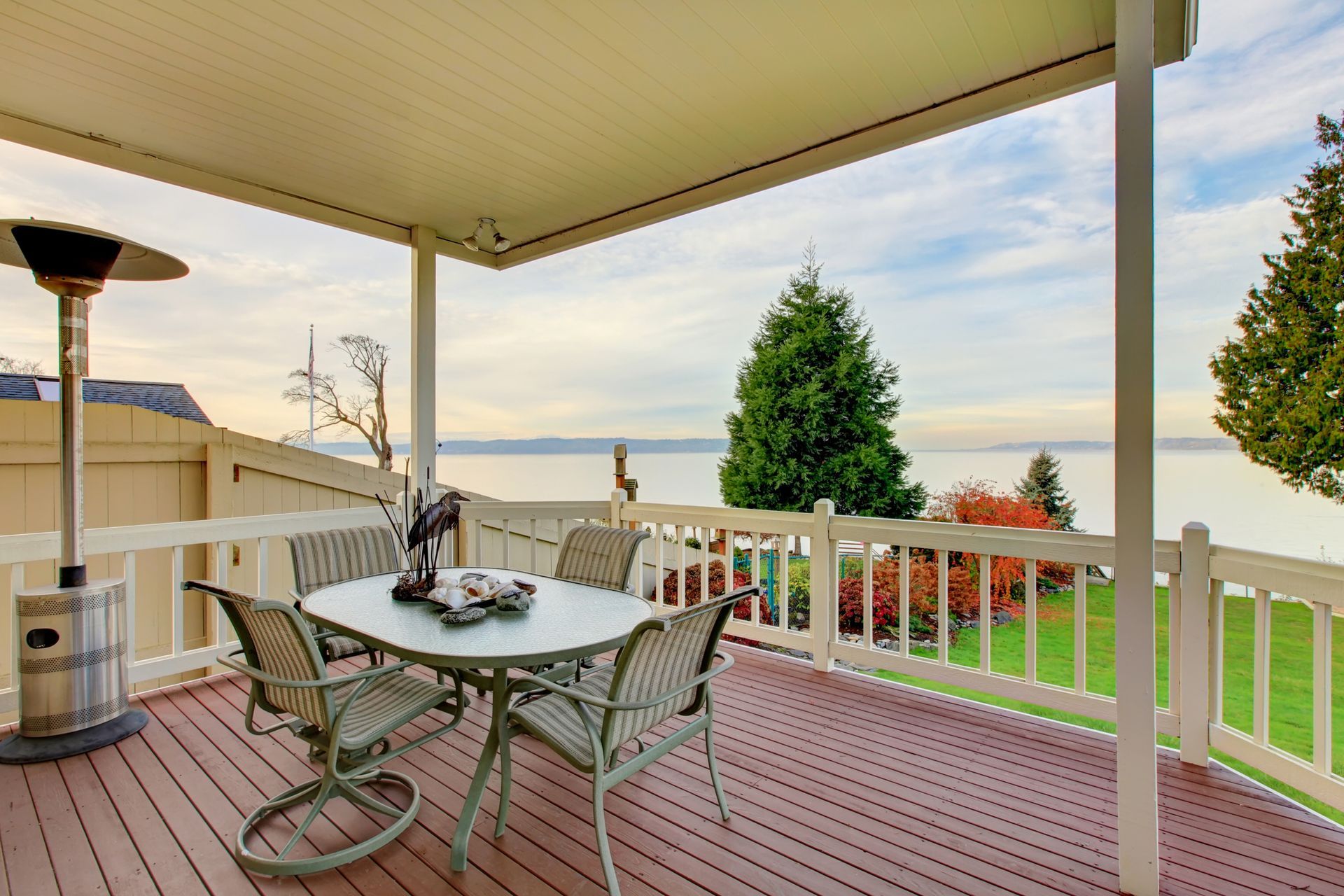 Patio with table, chairs, and heater overlooking water and landscape.