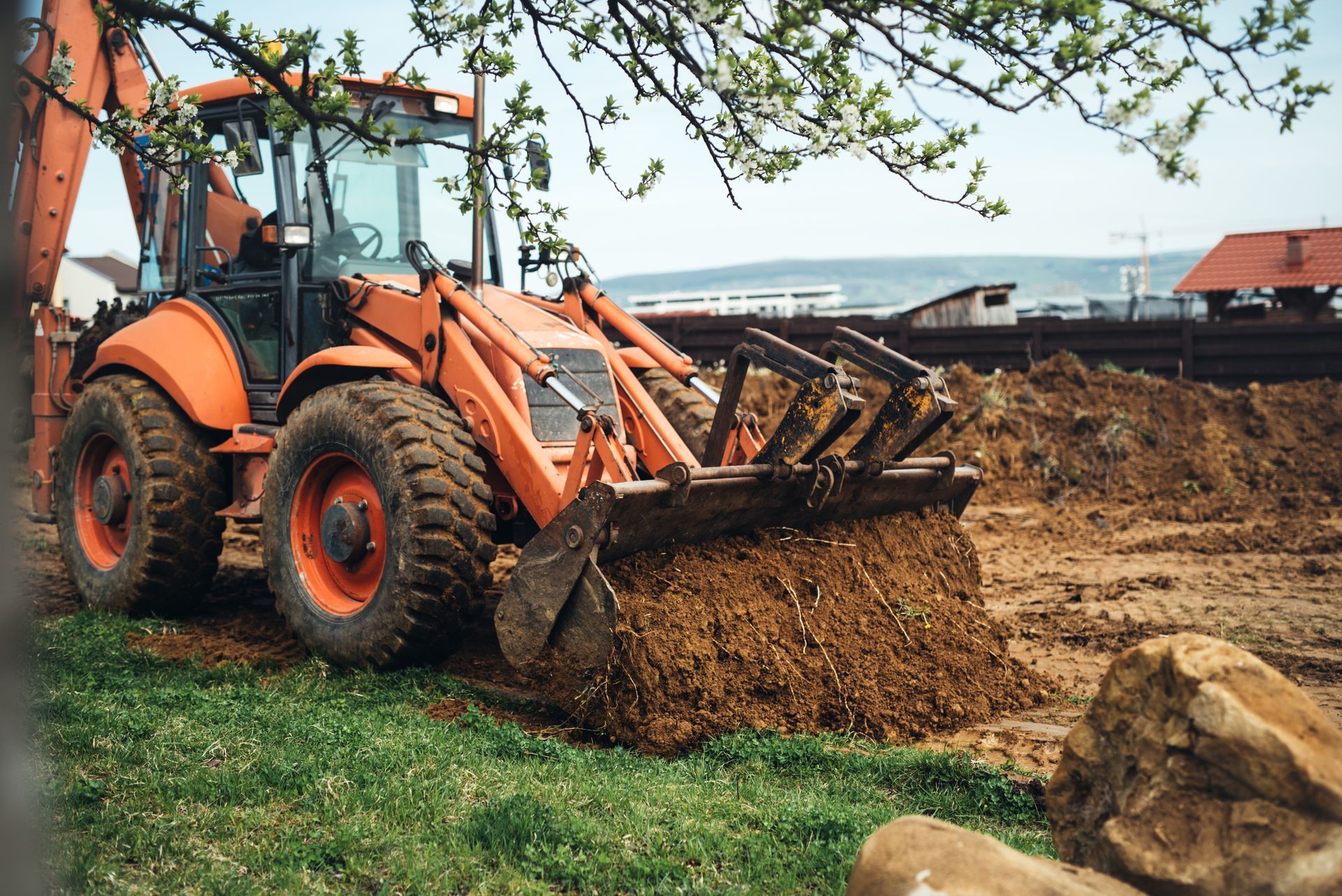 Orange backhoe scooping dirt on a construction site with green grass and cloudy sky.