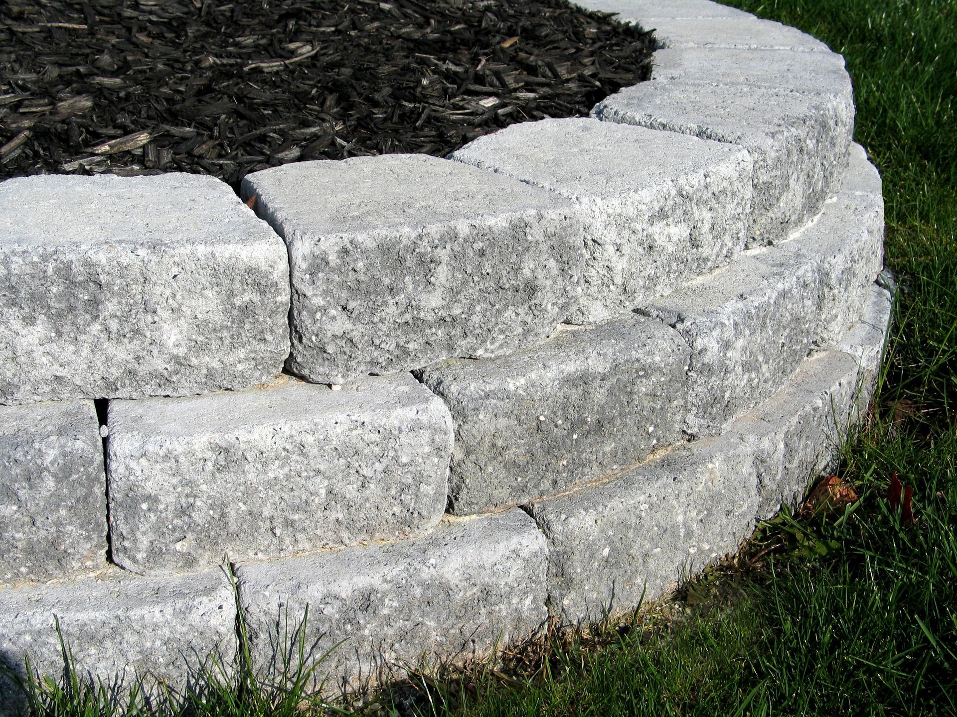 Gray stone retaining wall curving around a garden bed filled with dark mulch.