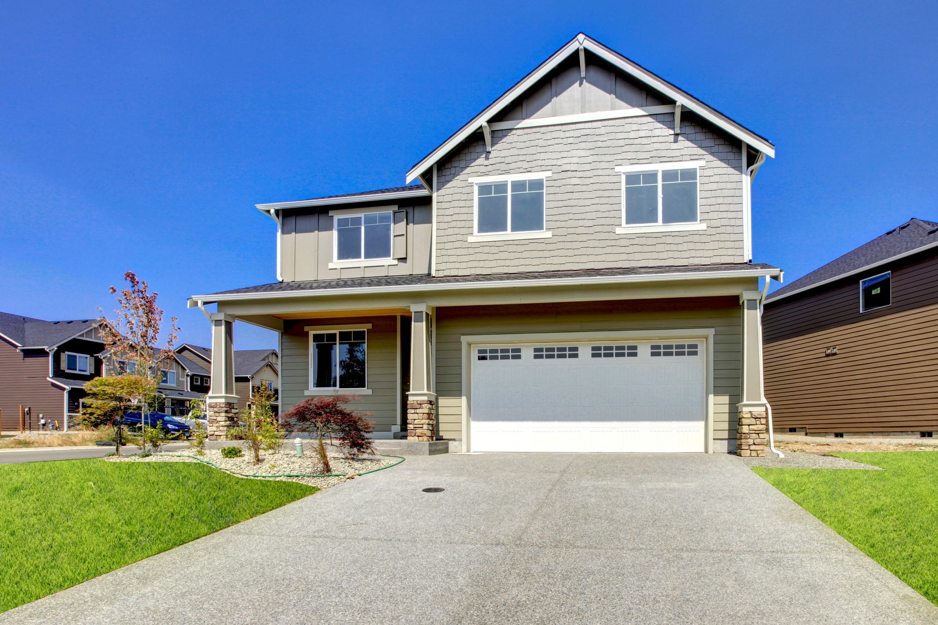 Two-story house with a white garage door and concrete driveway under a clear blue sky.