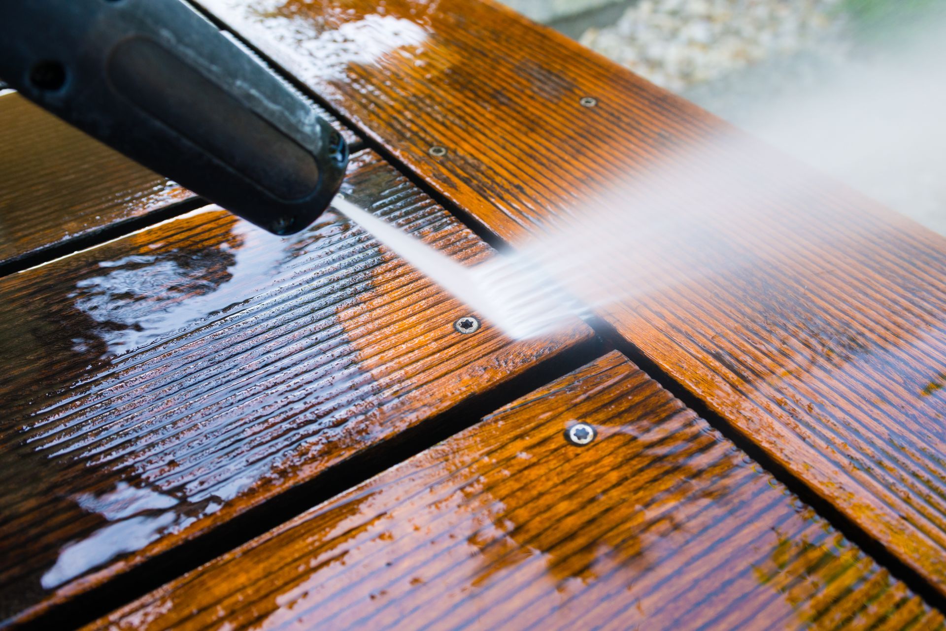 Pressure washer cleaning a wooden deck, spraying water, showing wet wood, outdoor setting.