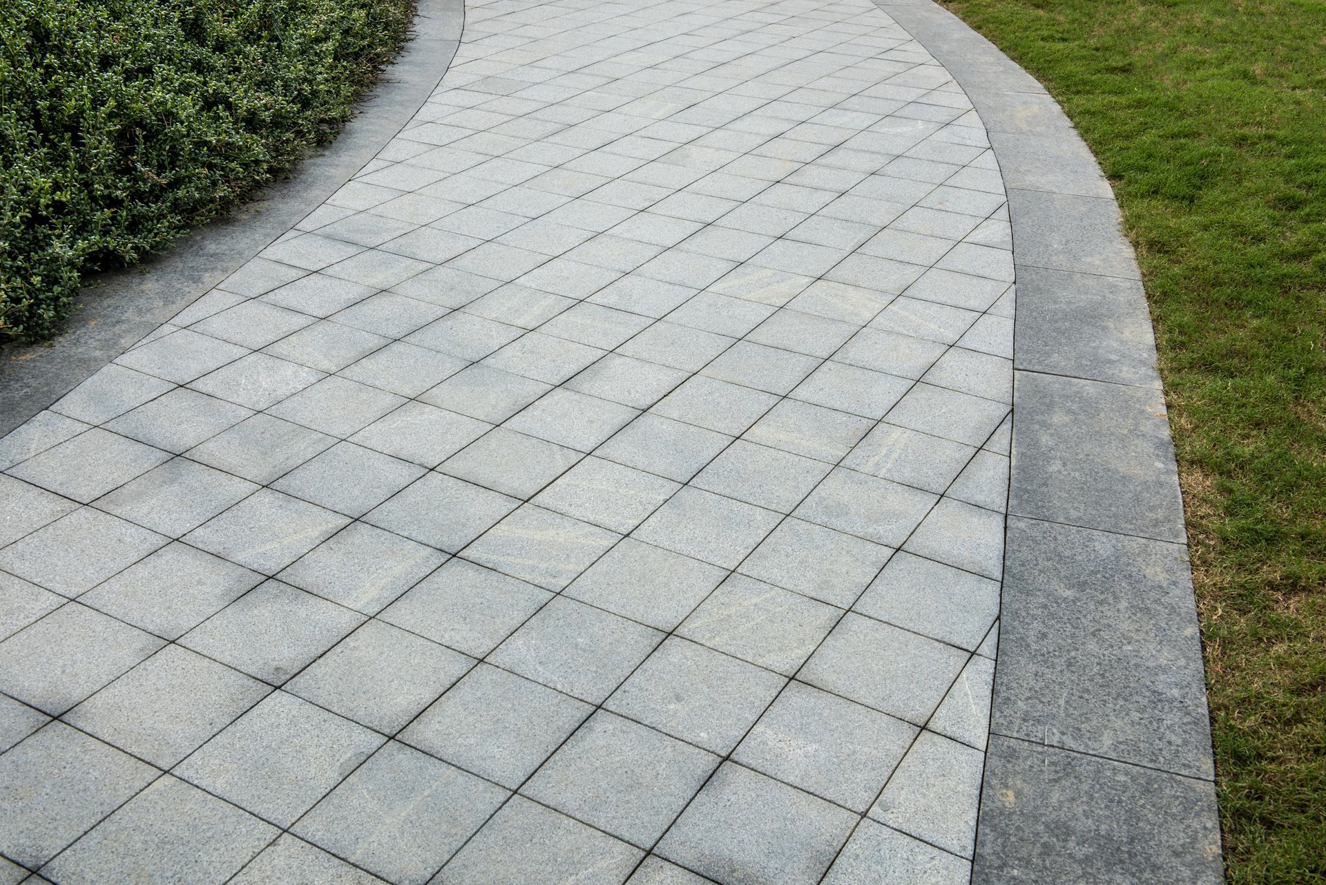 Gray brick pathway with grass and bushes.