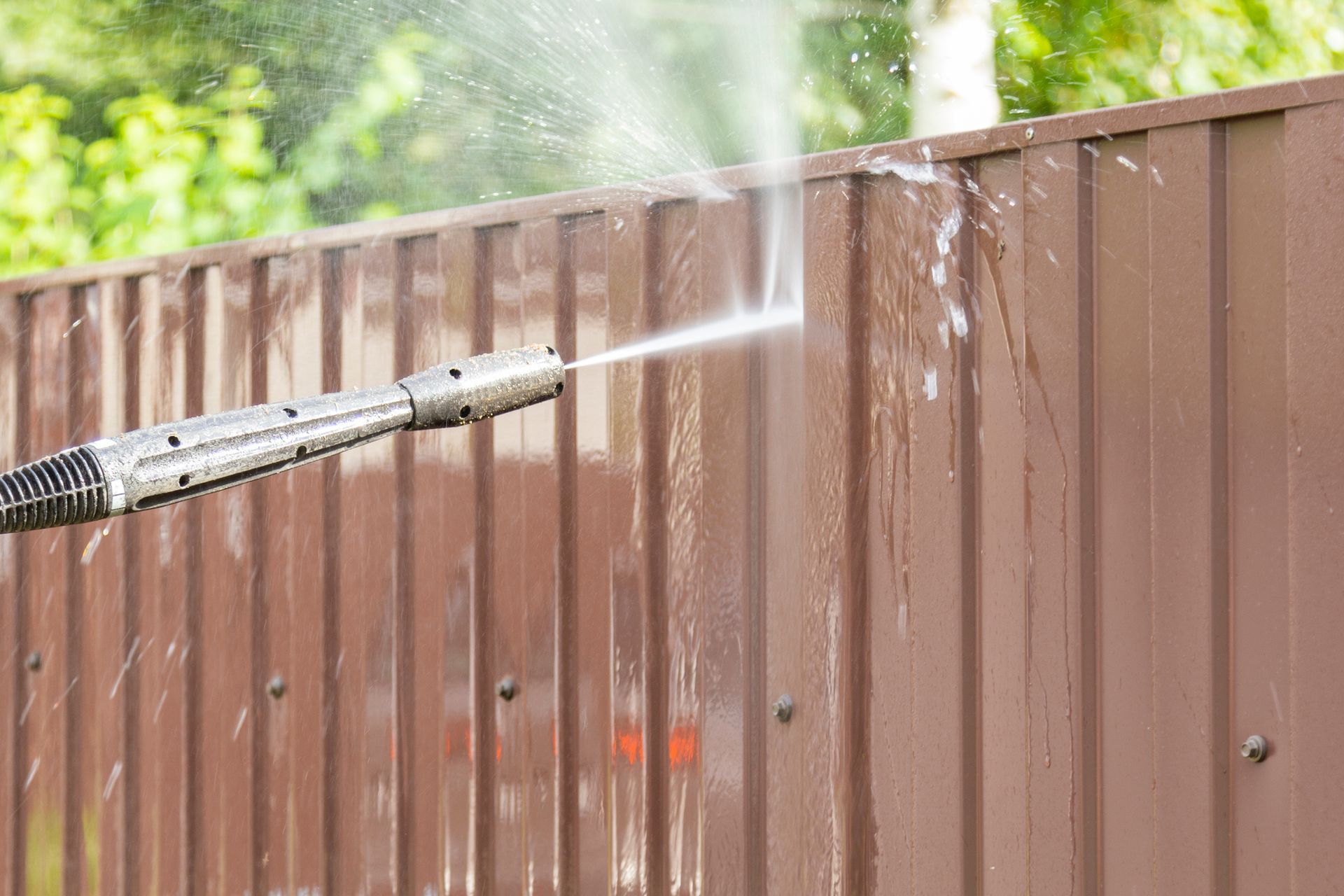 Pressure washing a brown metal fence outdoors.