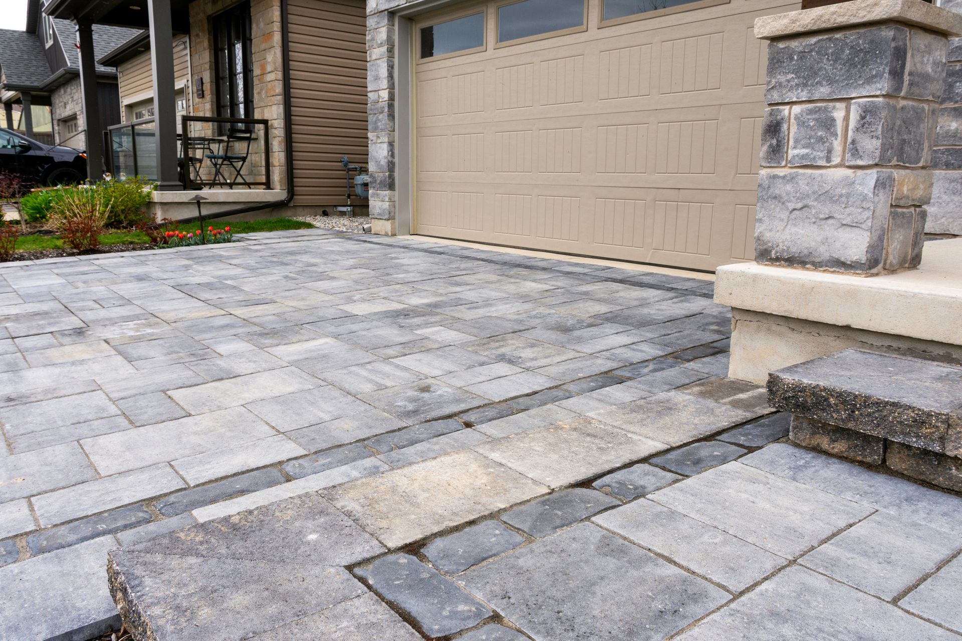 Paver driveway with a drain, leading to a tan garage door and house exterior with stonework.