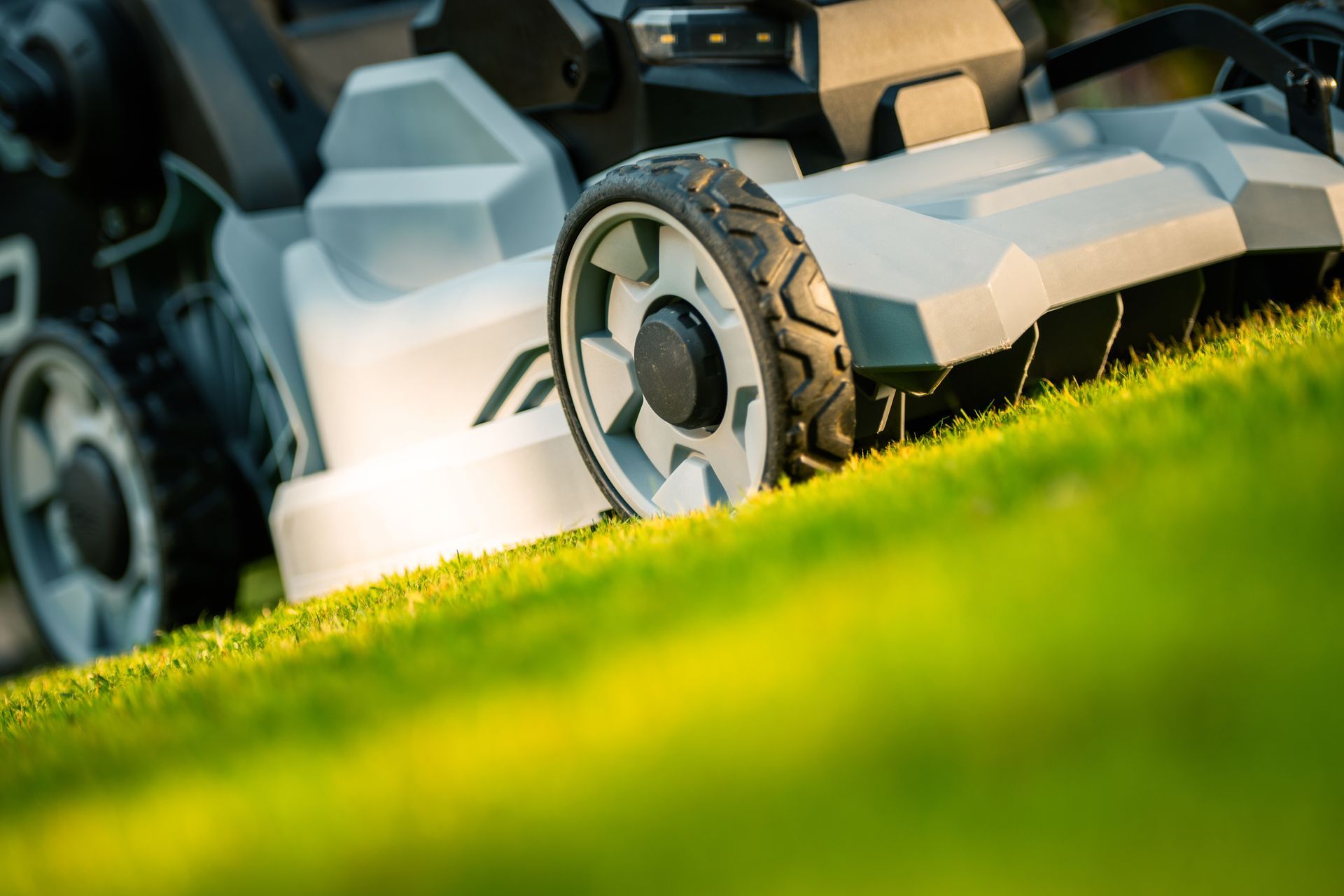 Lawnmower cutting green grass on a slight incline, close-up view.