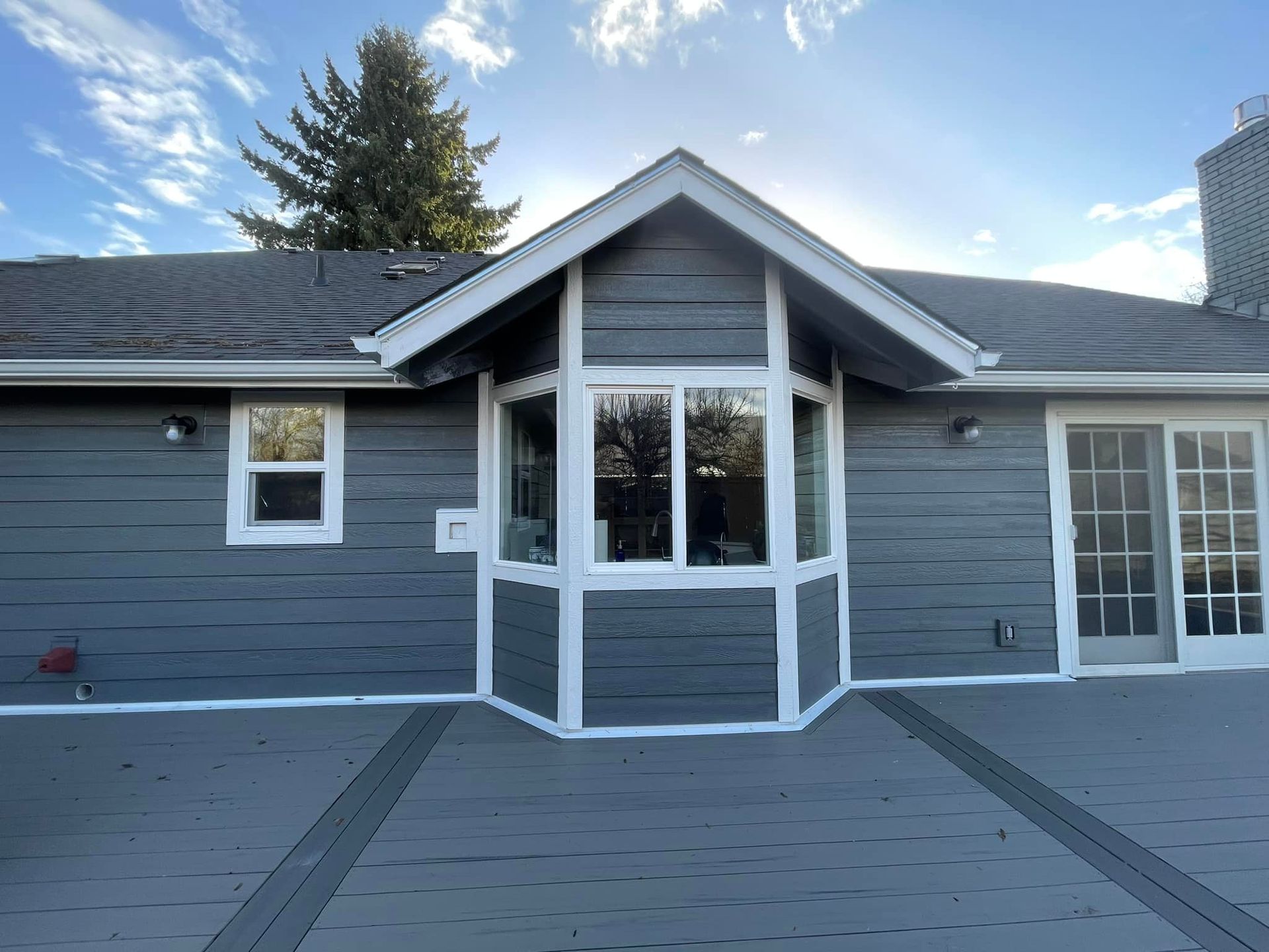 A gray house with a white trim and a large window.