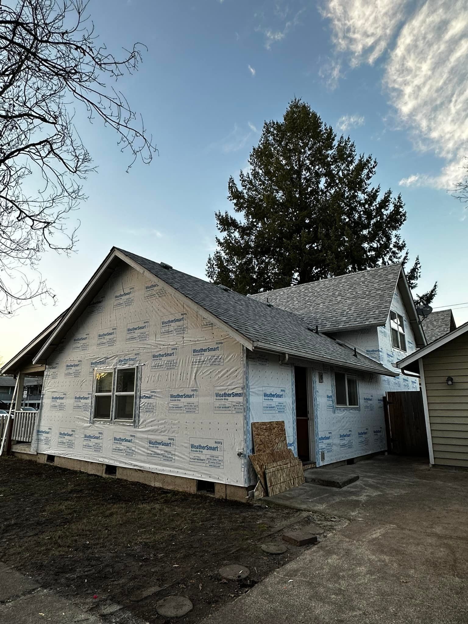 A white house with a gray roof and a tree in the background.