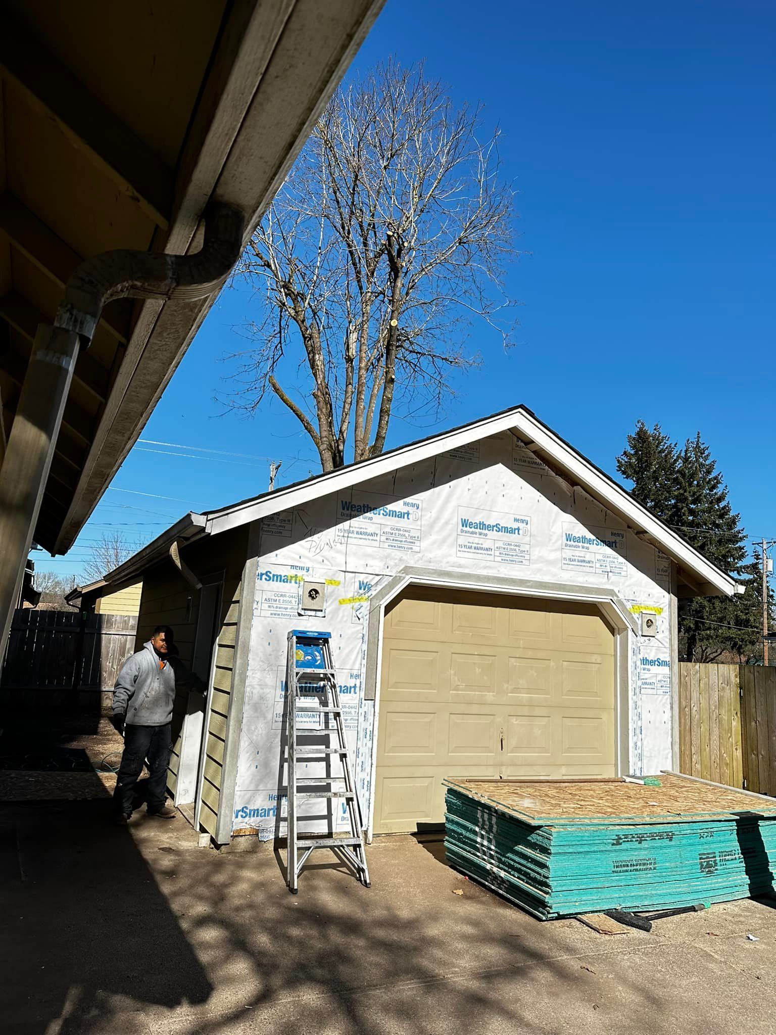 A garage is being remodeled with a ladder and a tree in the background.