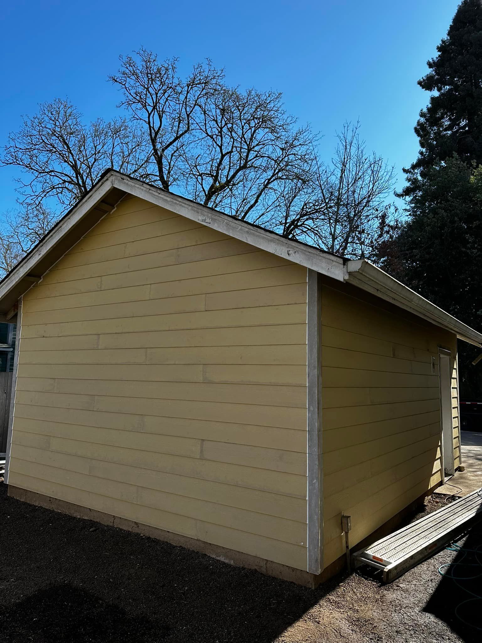 A small yellow shed with a roof and trees in the background.