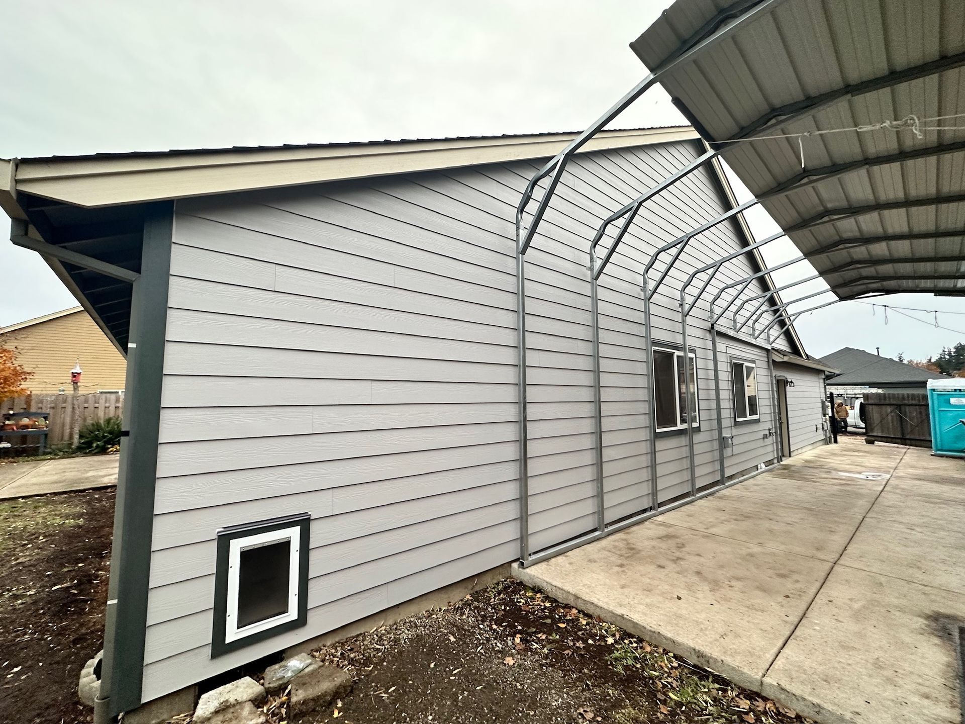 A house with a carport and a cat door on the side of it.