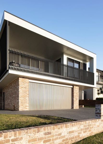 Modern two-story home with a brick base and balcony with black railing. Cream-colored garage door.
