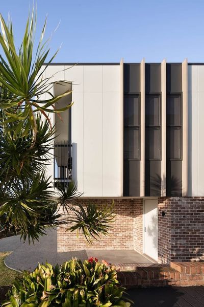 Modern home exterior with white siding, brick base, and dark vertical window accents.