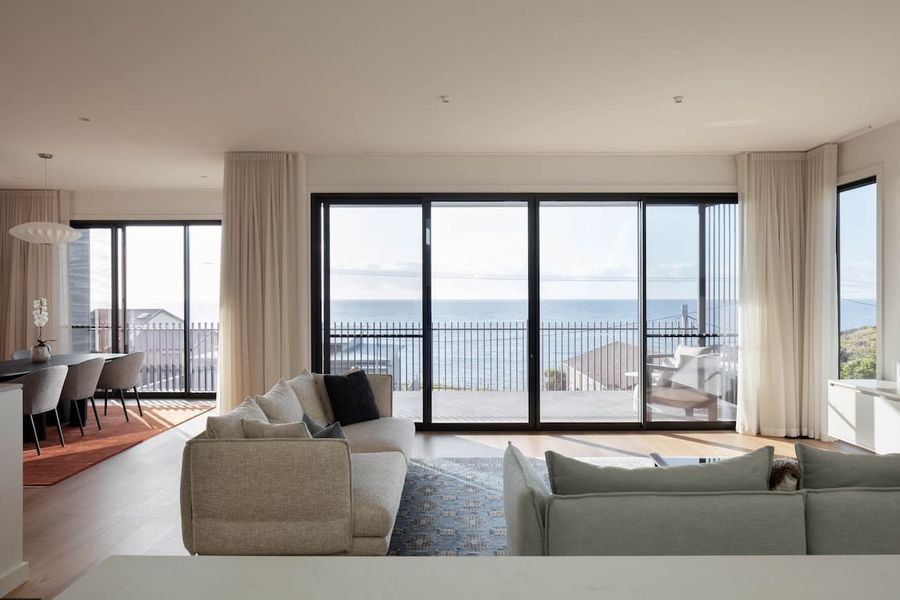 Spacious living room with ocean view, large windows, beige sofa, and neutral tones.