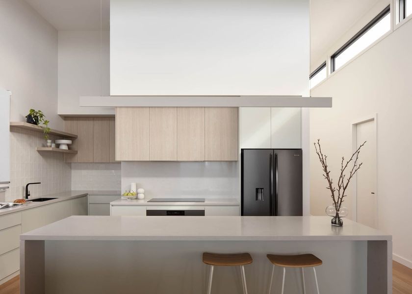 Modern kitchen with light wood cabinets, island with stools, and black refrigerator.