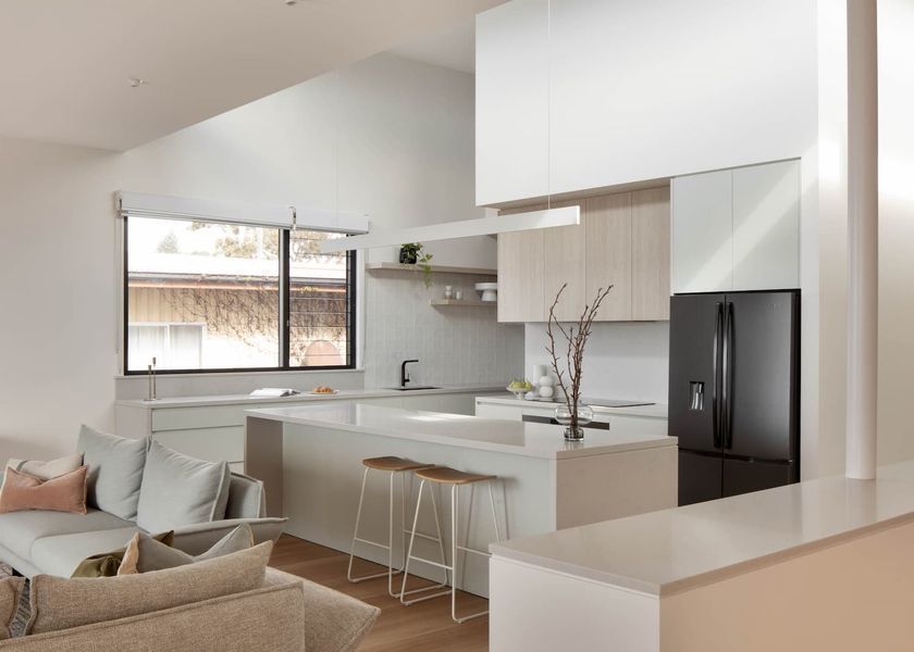 Modern kitchen with white cabinets, island, and black refrigerator. Includes a couch and window.