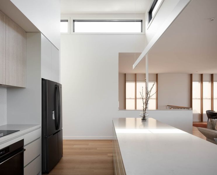 Modern kitchen with white cabinets, island, black fridge, and view to living room with window.