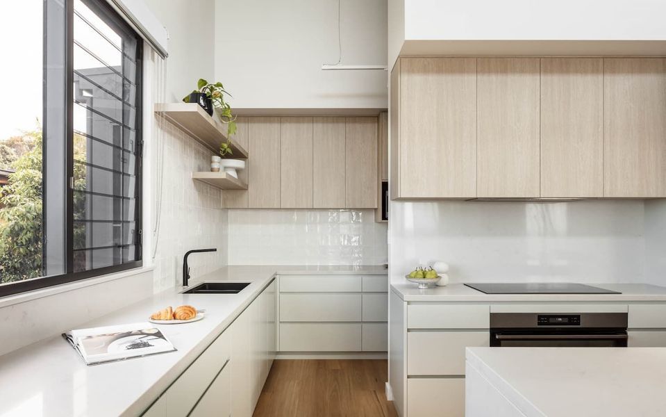 Modern kitchen with light wood cabinets, white counters, and black accents.