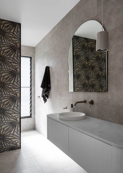 Modern bathroom with gray tile walls, a patterned accent wall, and an arched mirror over a floating vanity.